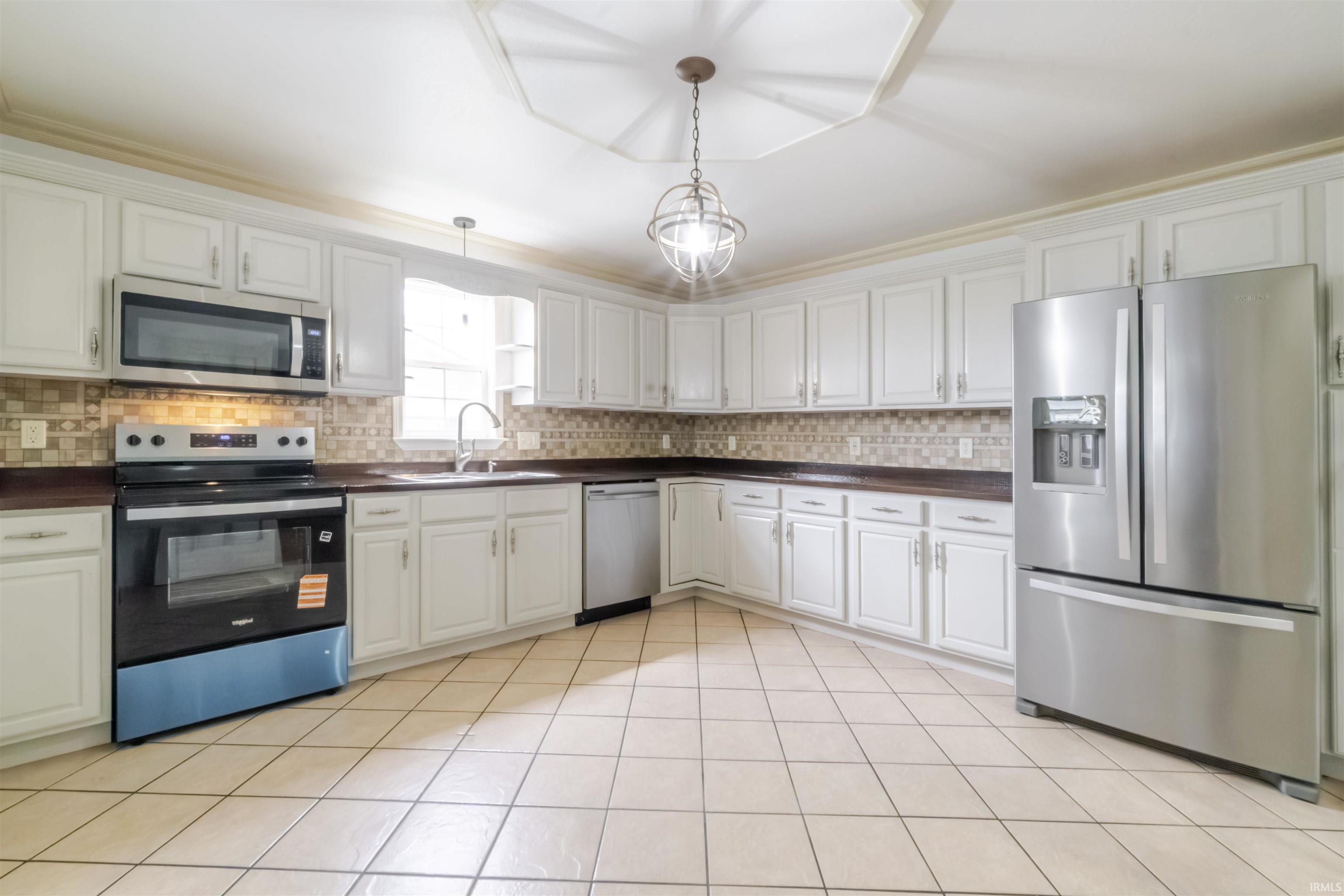 Kitchen featuring stainless steel appliances, dark countertops, white cabinetry, decorative backsplash, and ornamental molding