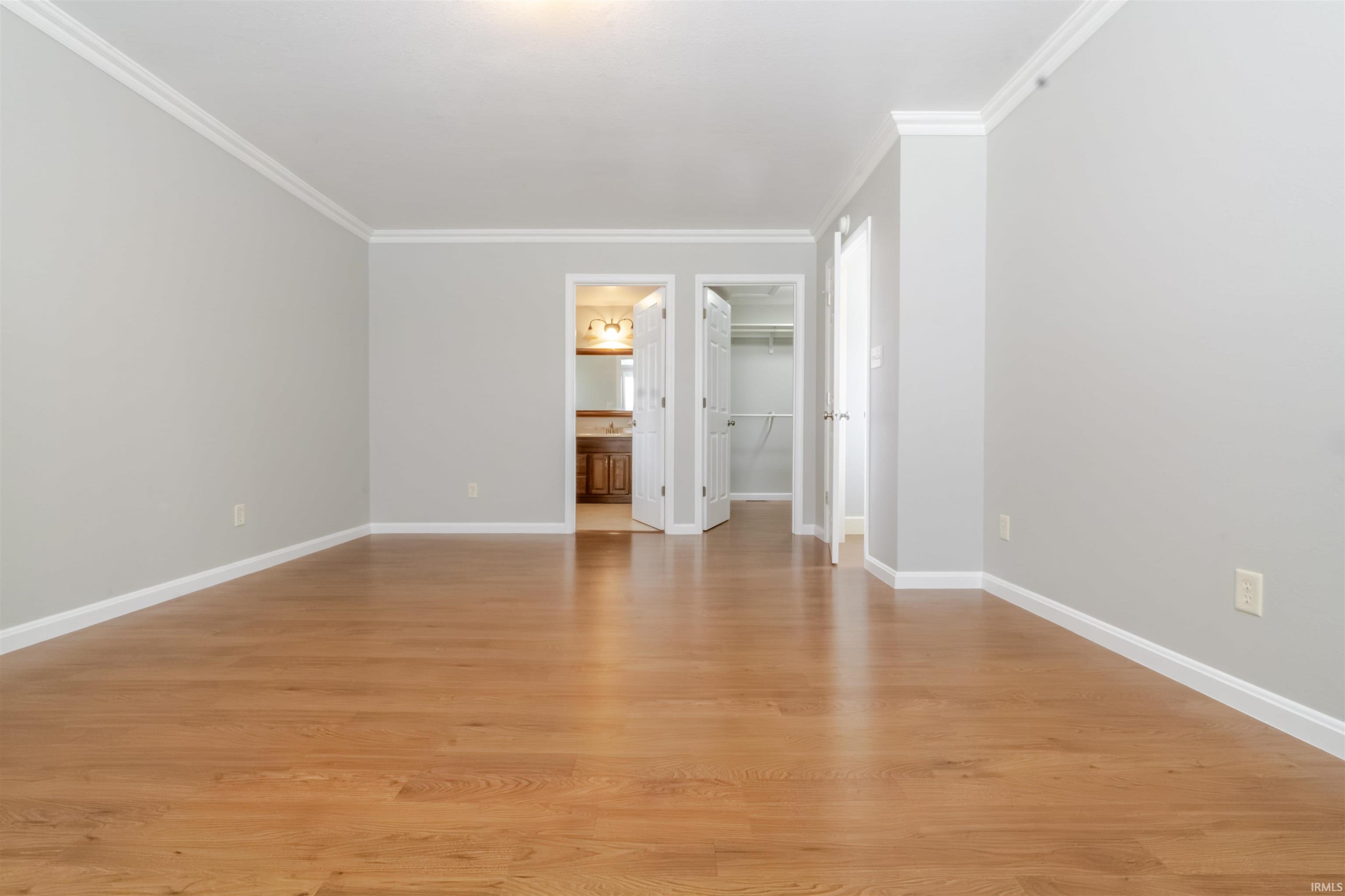 Unfurnished bedroom featuring a walk in closet, light wood finished floors, ornamental molding, and ensuite bathroom