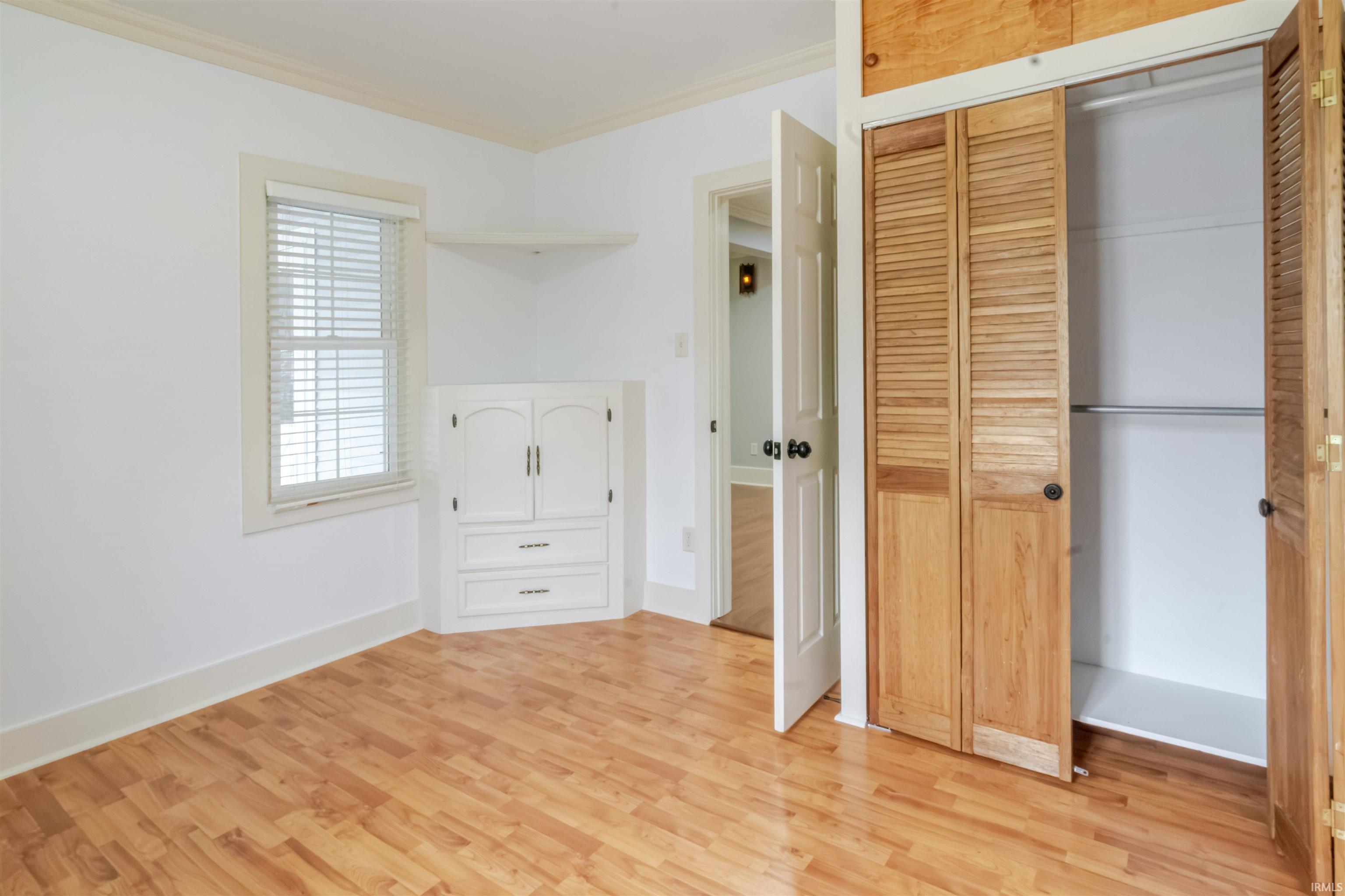 Unfurnished bedroom featuring crown molding, light wood-type flooring, and a closet