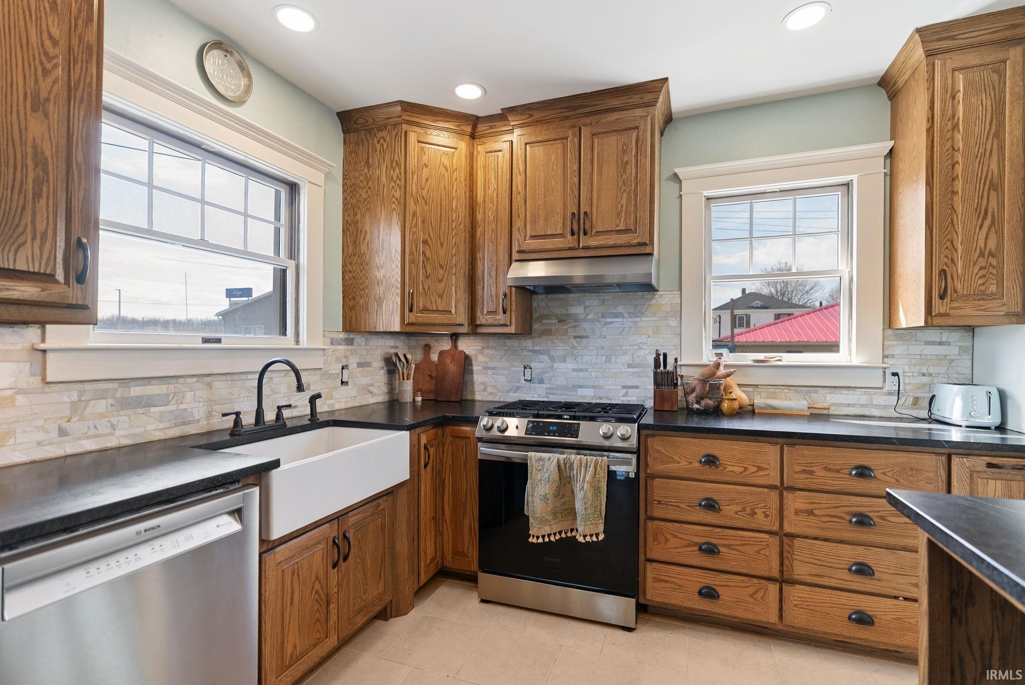 Kitchen featuring wood finish cabinetry, stainless steel appliances, exhaust hood, recessed lighting, and decorative backsplash