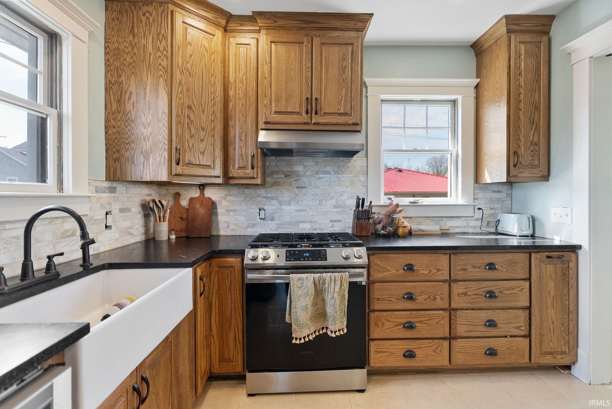 Kitchen with wood finish cabinets, stainless steel gas stove, range hood, and tasteful backsplash