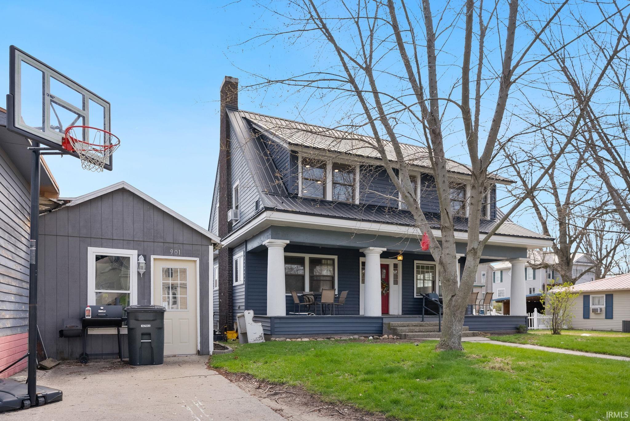 View of front of property featuring a front yard, covered porch, a chimney, and a metal roof