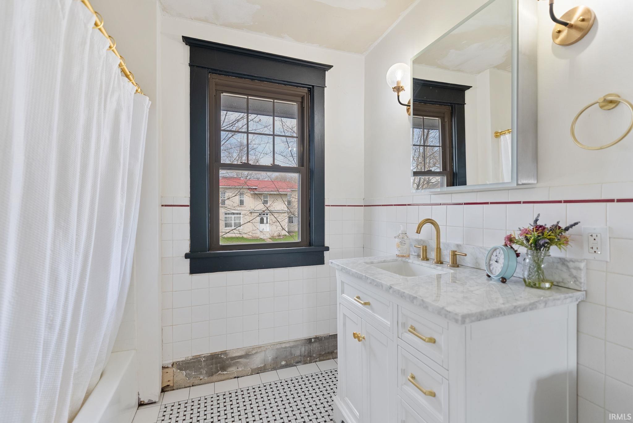 Bathroom featuring tile walls, vanity, a wainscoted wall, healthy amount of natural light, and shower / bath combination with curtain