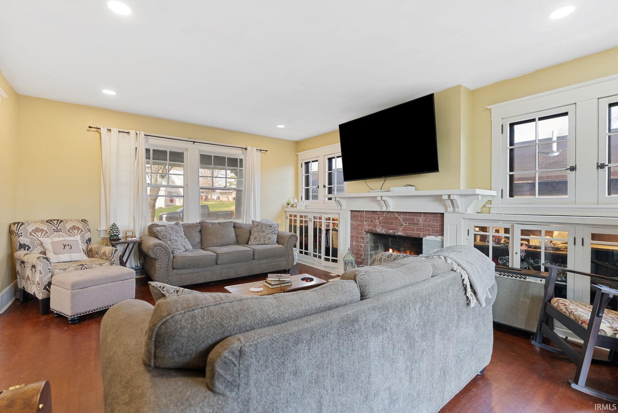 Living area with plenty of natural light, recessed lighting, a brick fireplace, and dark wood-type flooring