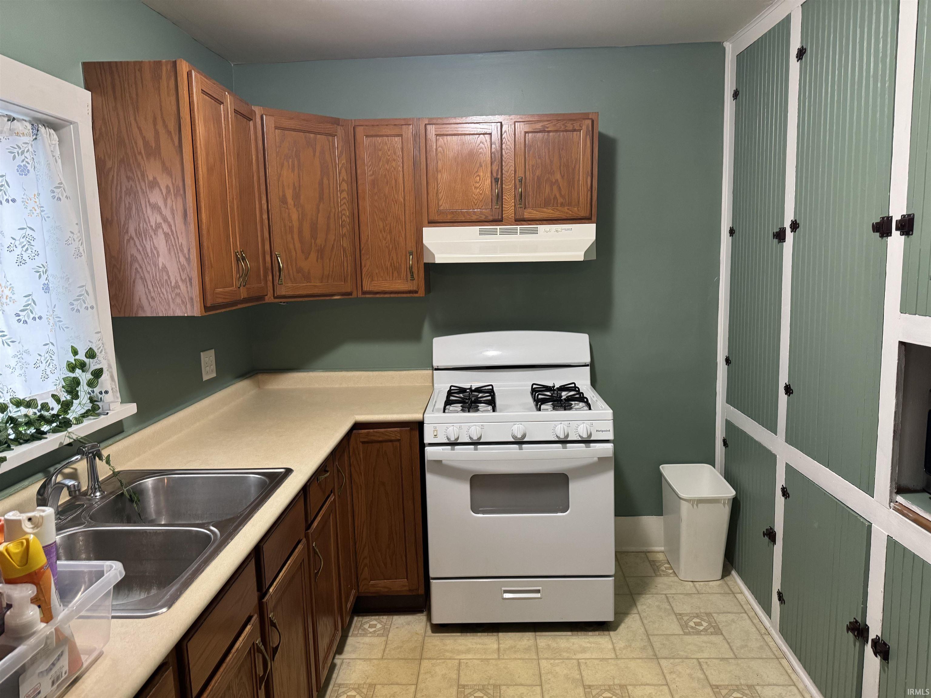 Kitchen featuring white range with gas cooktop, light countertops, stone finish flooring, and wood finish cabinets