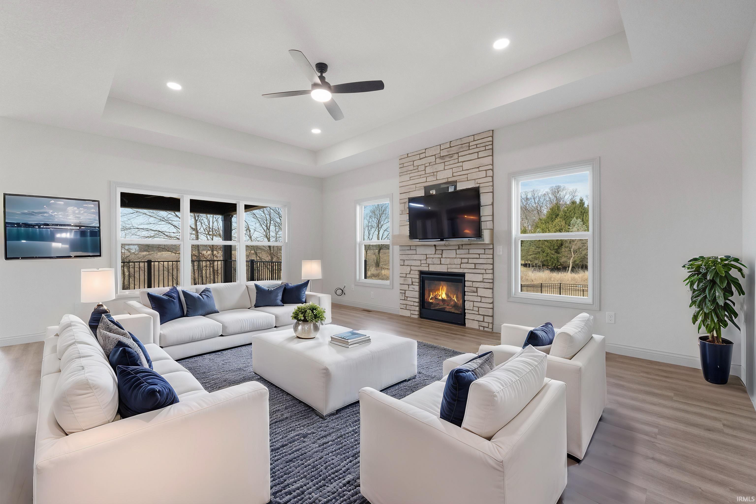 Living room featuring a stone-clad fireplace, wood-finish flooring, recessed lighting, a ceiling fan, and large windows