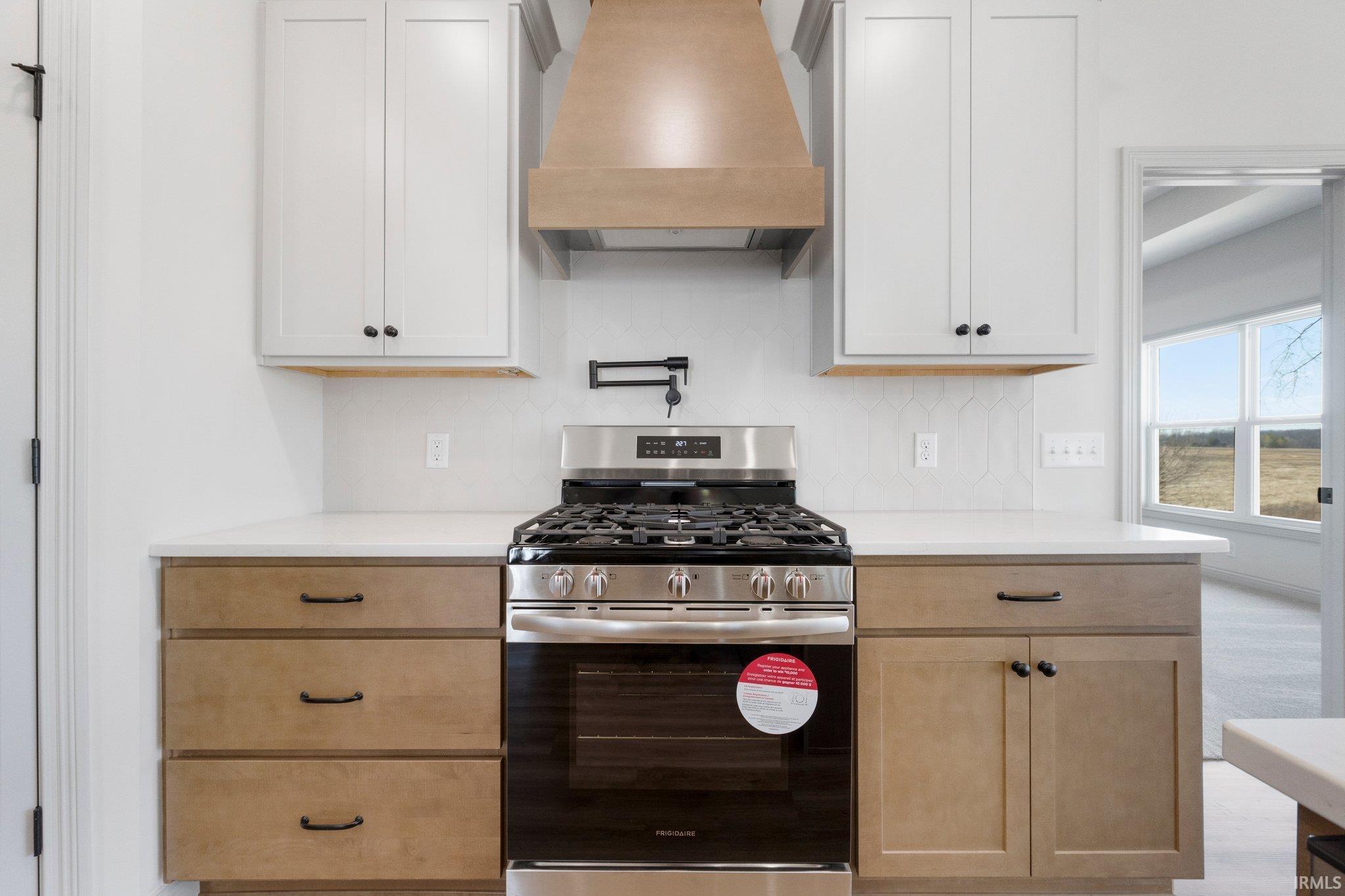 Gourmet kitchen featuring a stainless steel gas range, two-tone cabinetry with black hardware, white countertops, and a decorative wood-finish range hood
