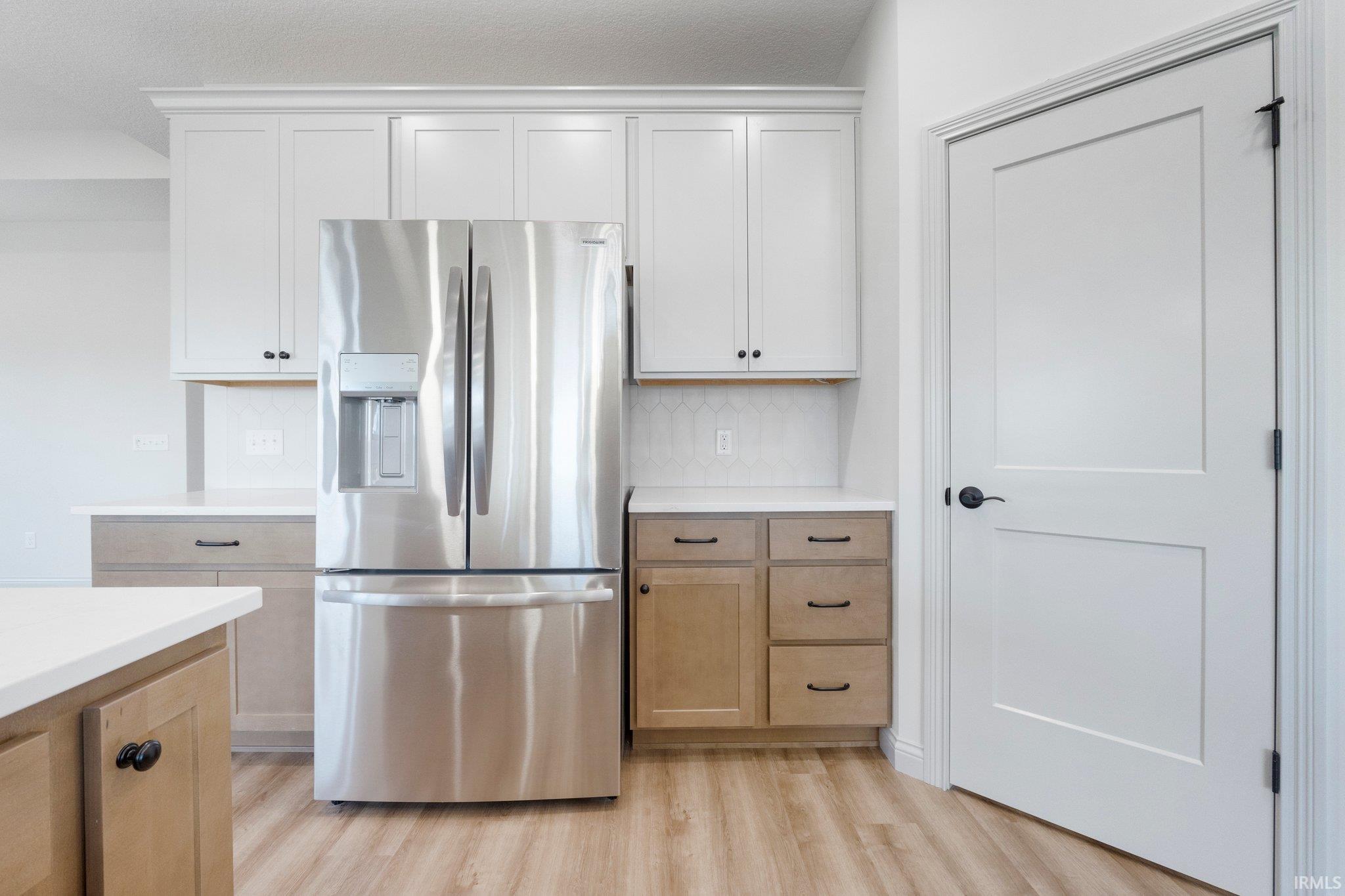 Stainless steel French door refrigerator set amidst white and natural wood-finish cabinetry