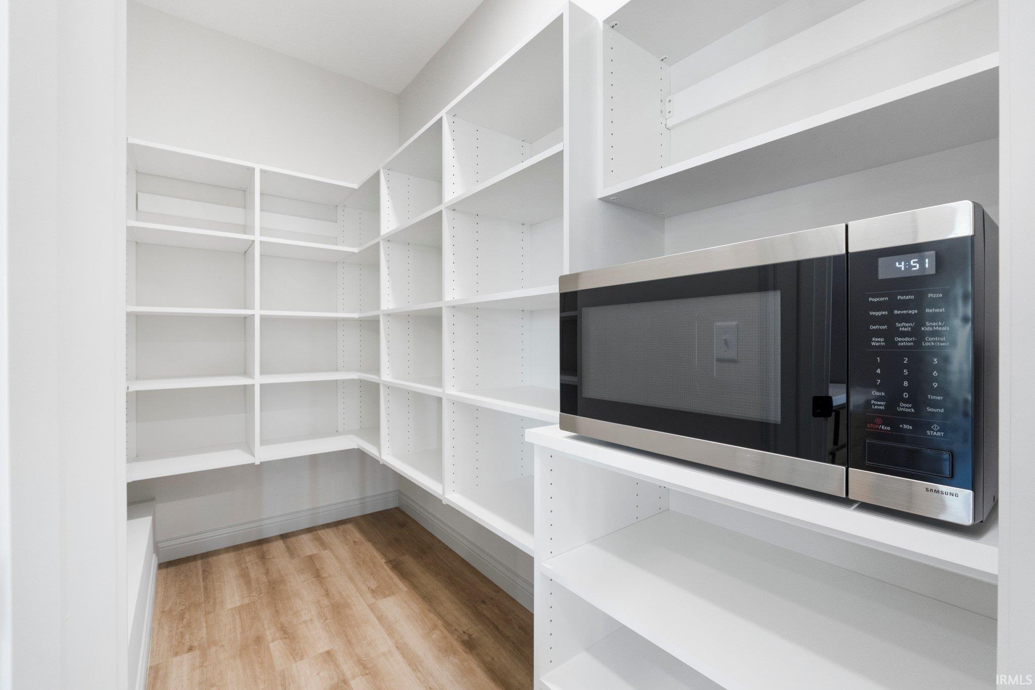 Walk-in pantry featuring extensive white shelving, wood-finish flooring, and a built-in microwave