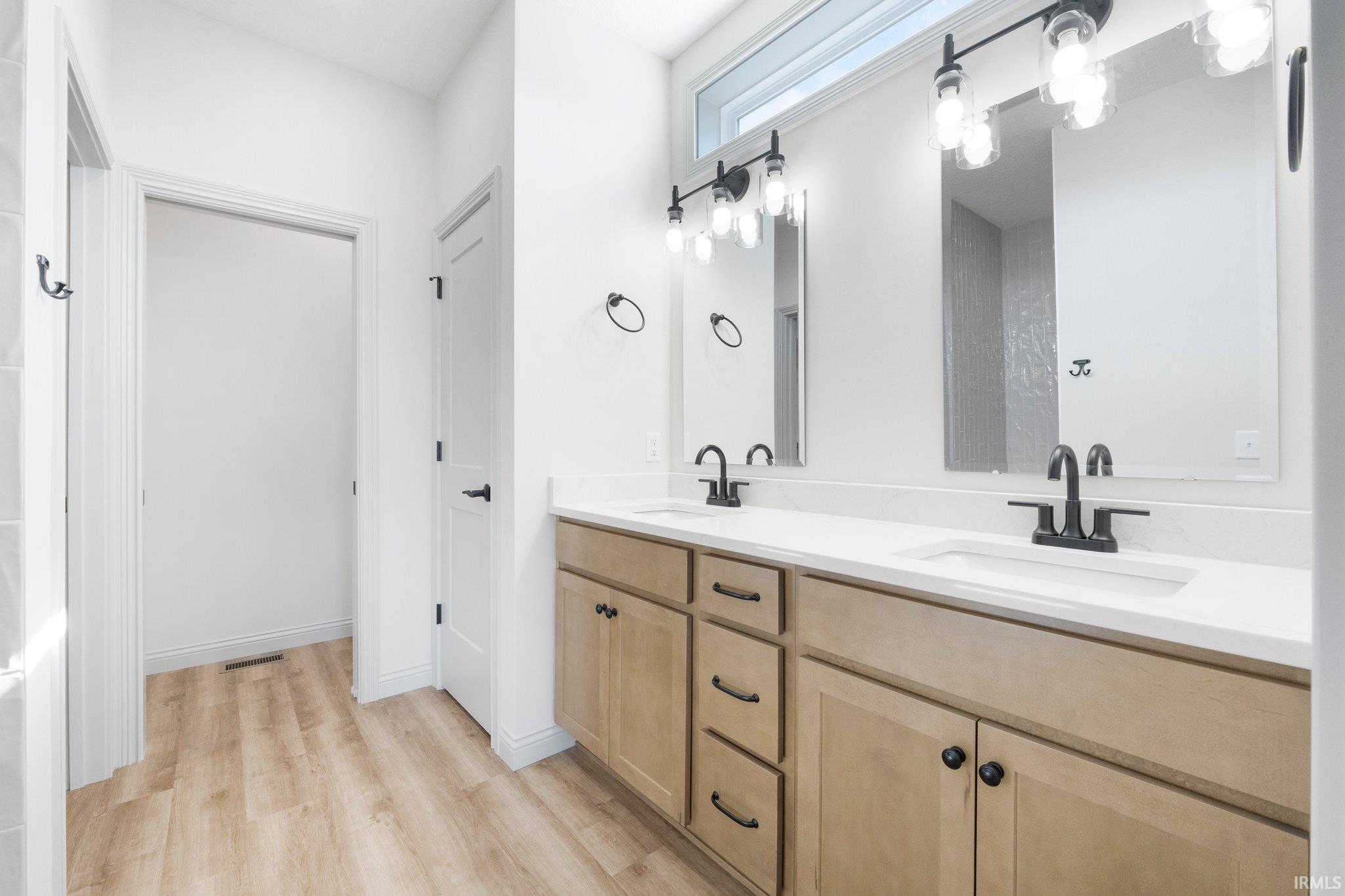 Double vanity featuring light wood-finish cabinetry, white countertops, and matte black fixtures