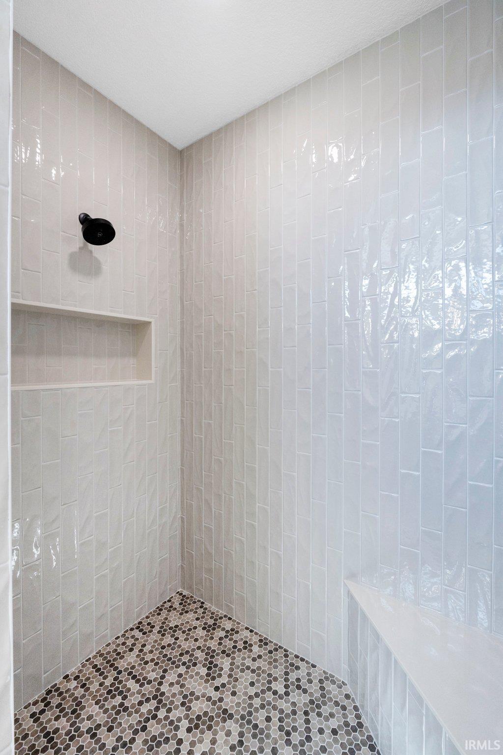 Shower stall featuring vertical subway tile walls, a built-in shower bench, and a mosaic tile floor