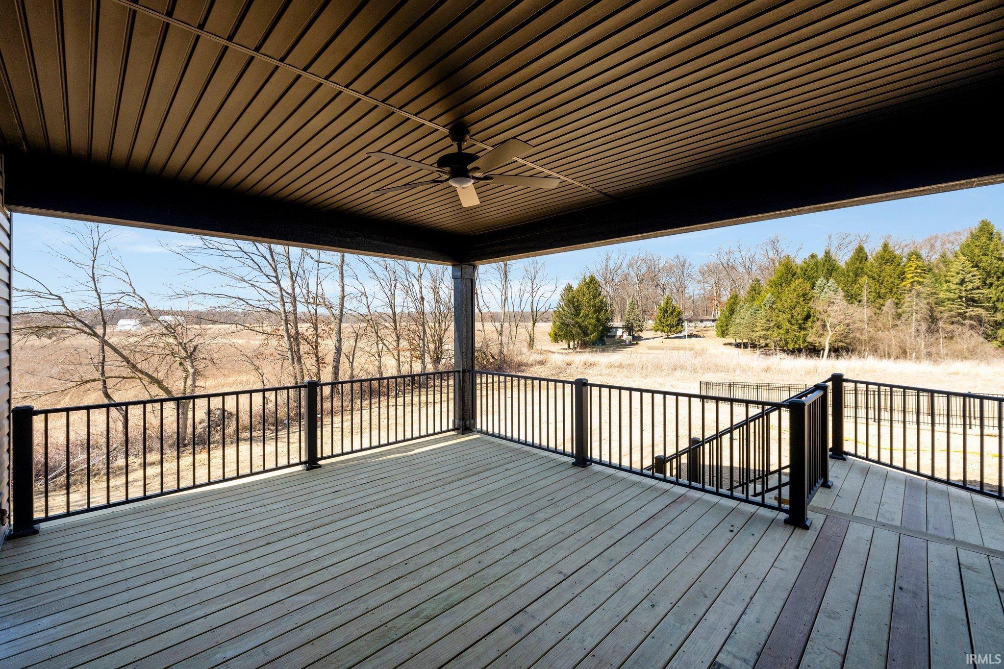 Expansive covered deck featuring wood-finish flooring, black metal railing, and a ceiling fan
