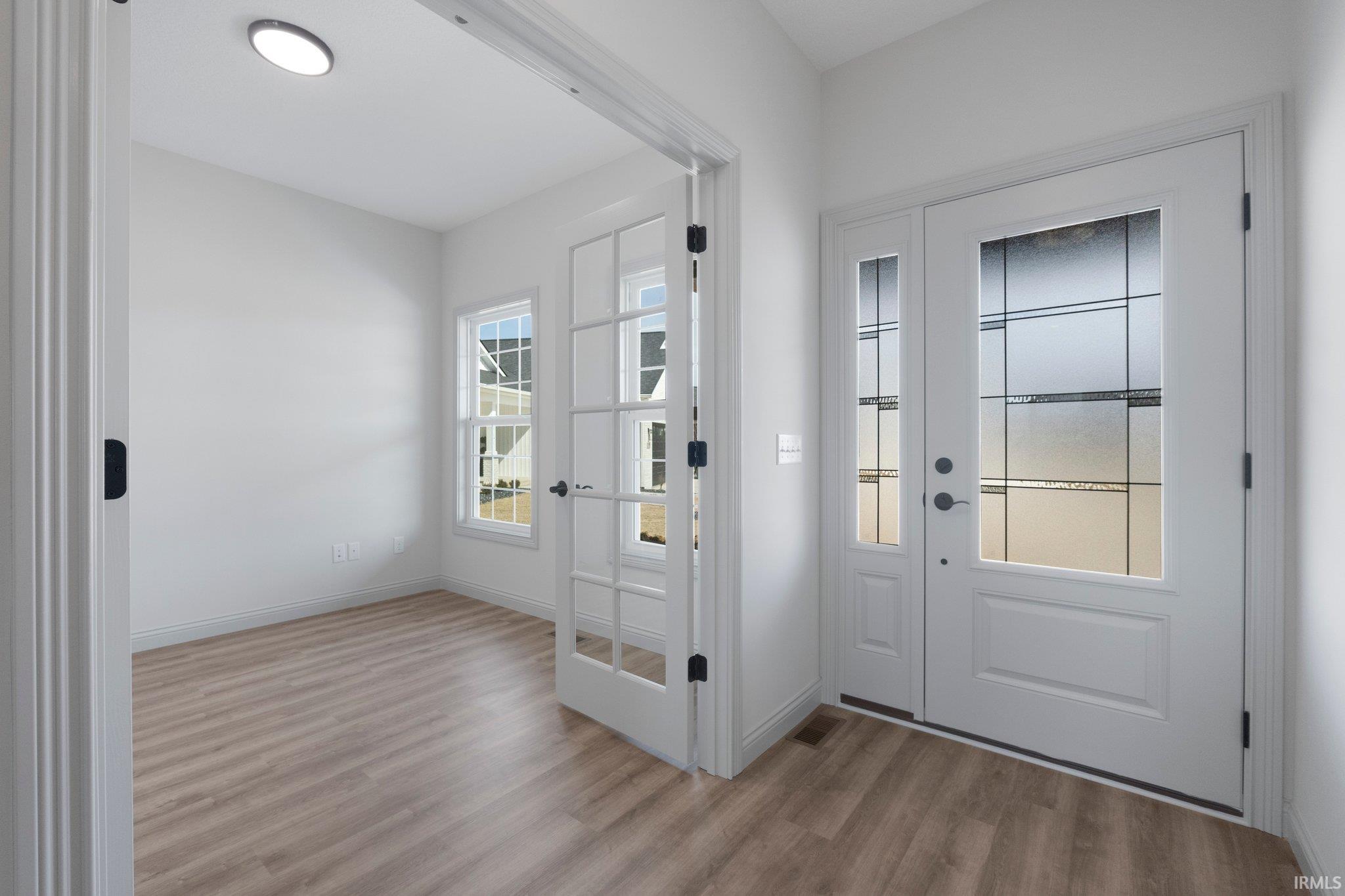 Foyer with wood-finish flooring, a white front door featuring decorative glass, and double French doors opening into a room with two windows and a recessed ceiling light