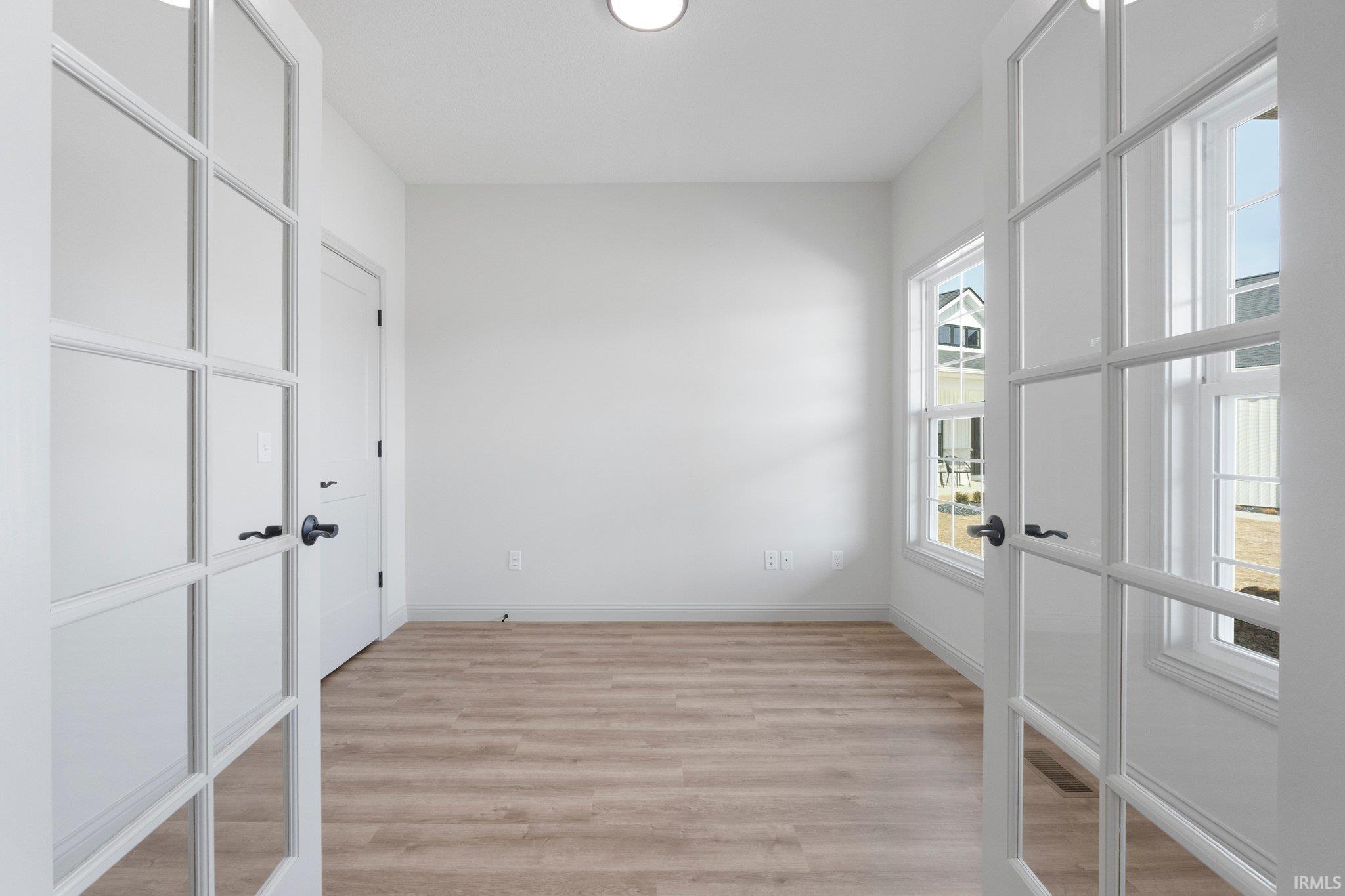 Bright room featuring two large windows, wood-finish flooring, and white walls