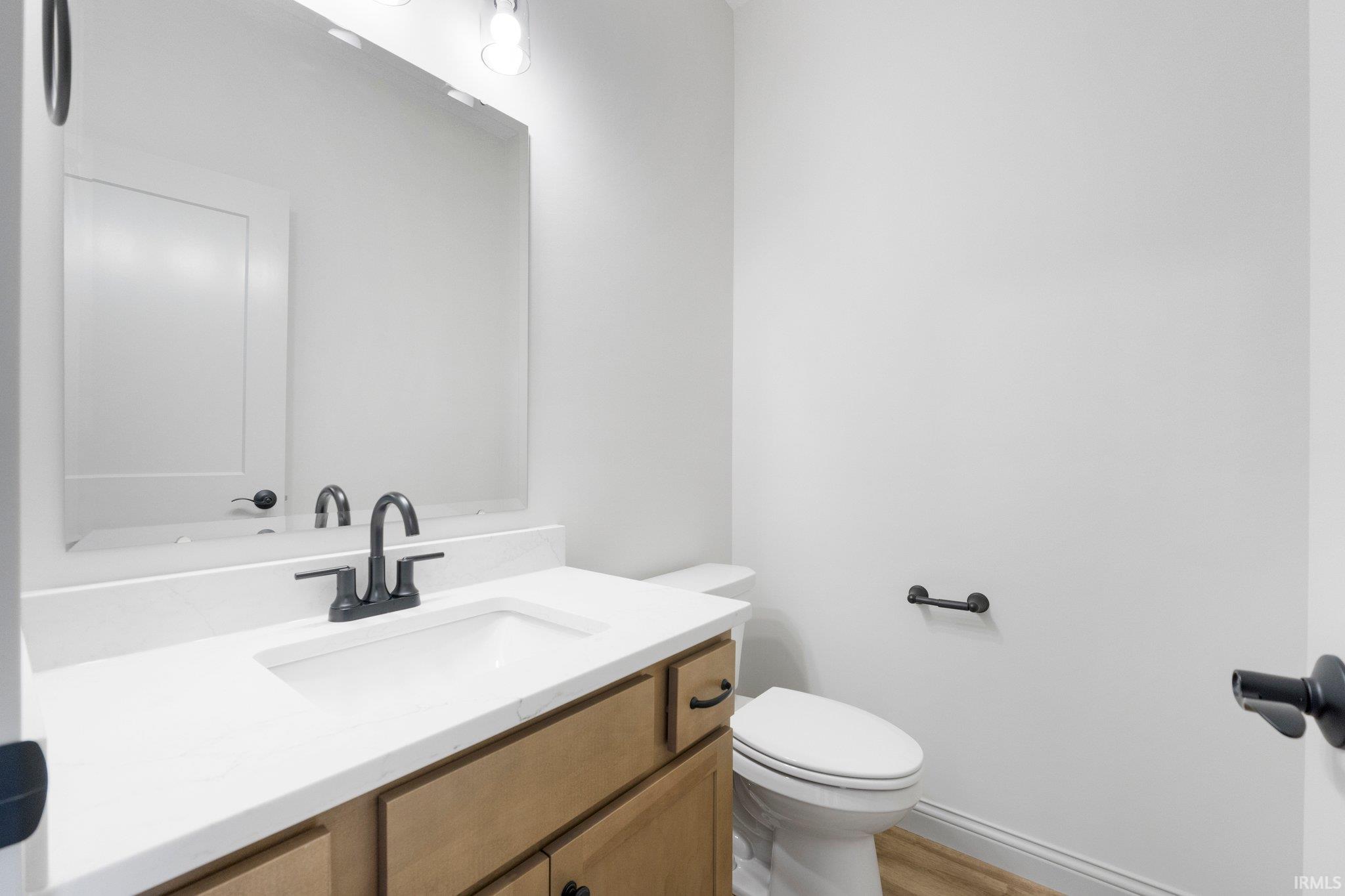 Modern bathroom vanity featuring light wood-finish cabinetry with black hardware, a pristine white countertop, and an undermount sink with a matte black faucet