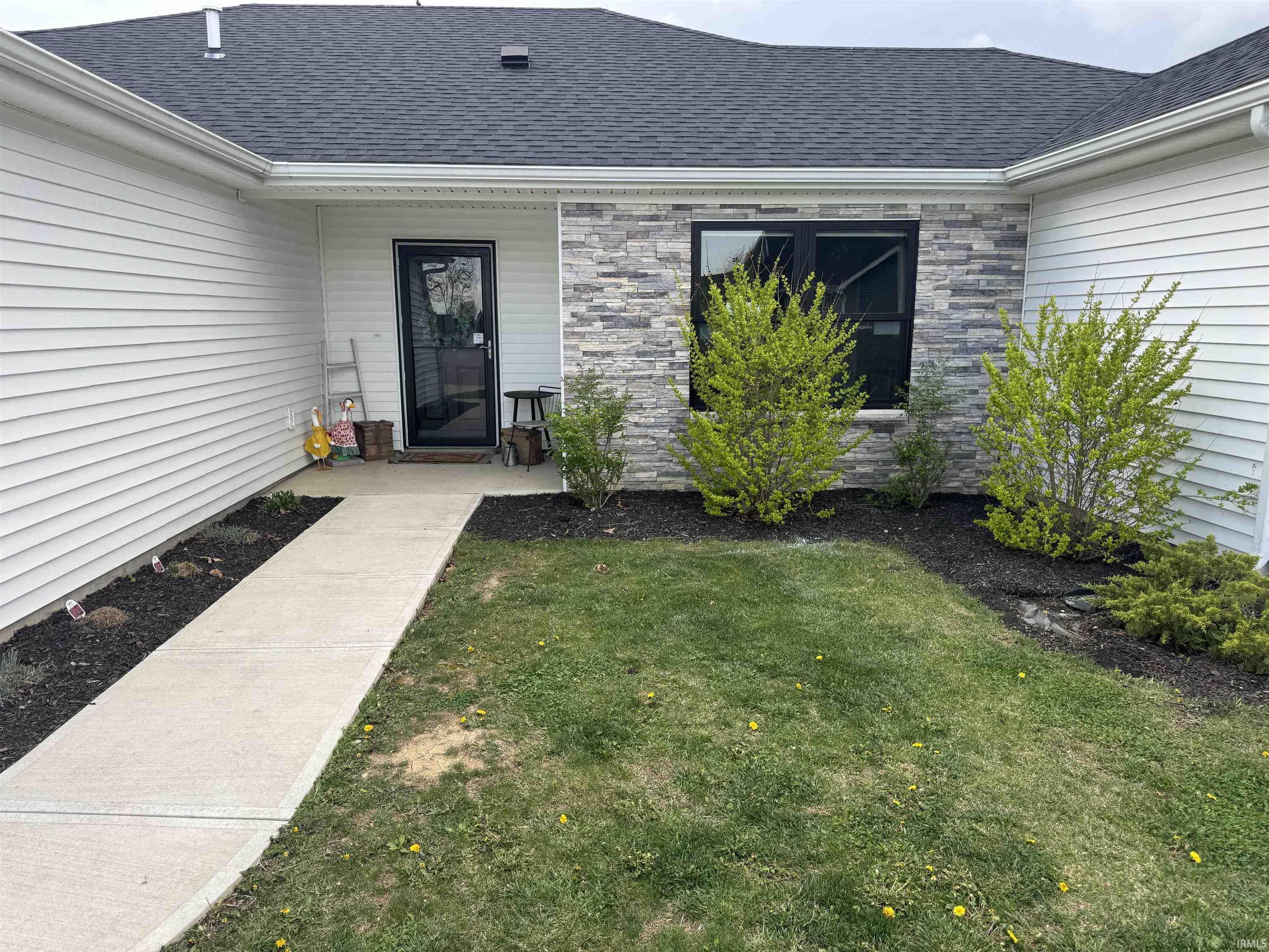 Property entrance featuring a lawn, roof with shingles, and stone siding