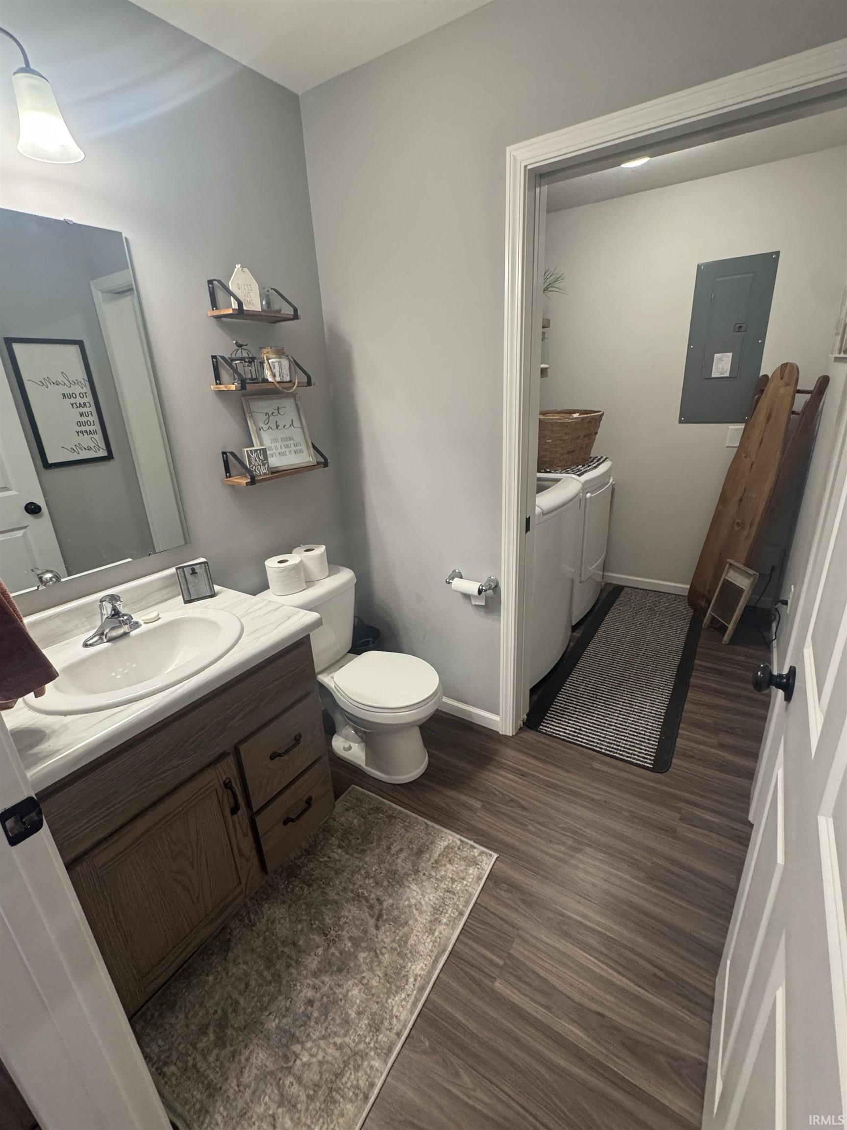 Half bath with vanity, washer and clothes dryer, electric panel, and dark wood-style floors