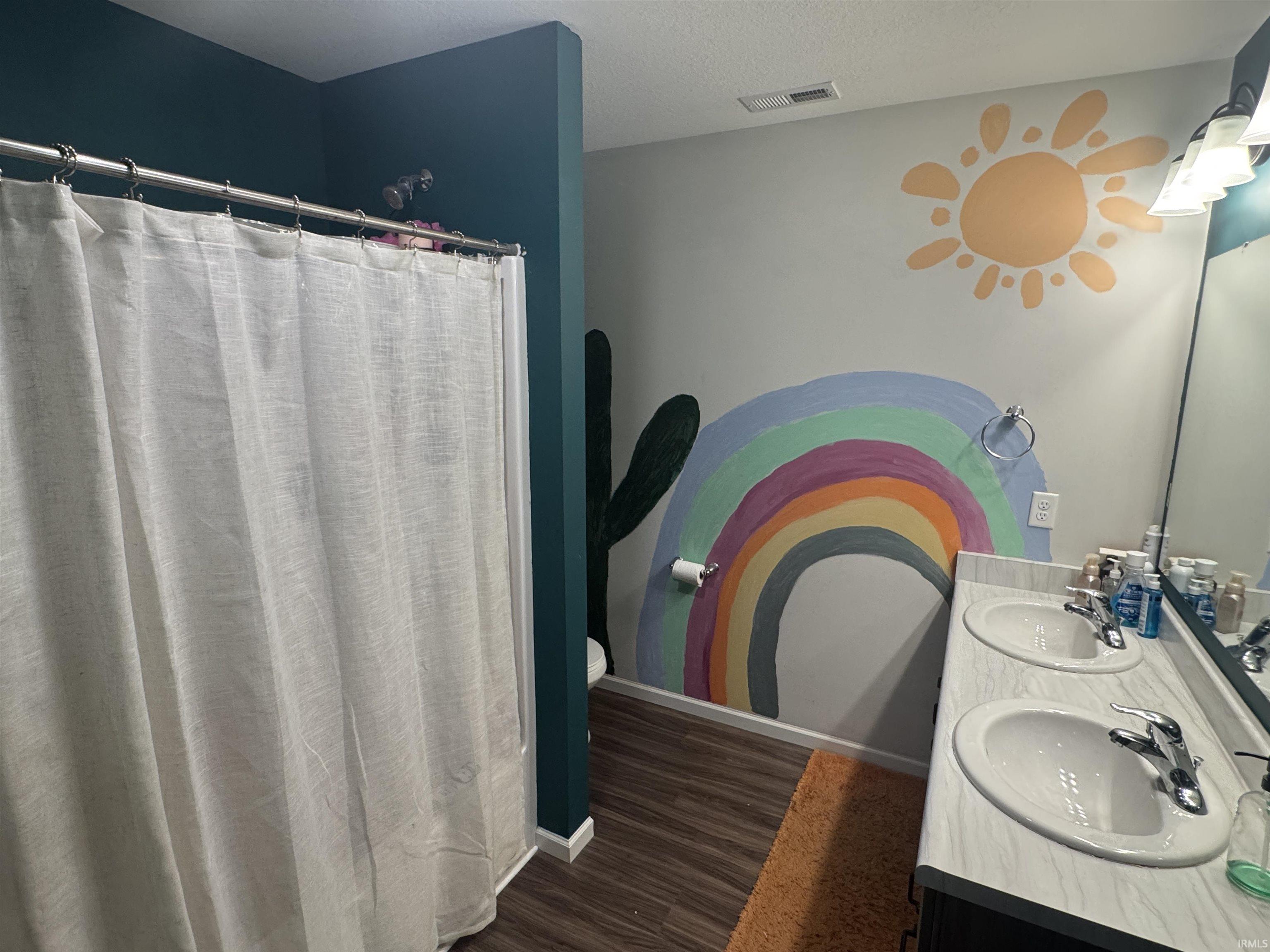 Full bath with double vanity, a shower with shower curtain, and dark wood-type flooring