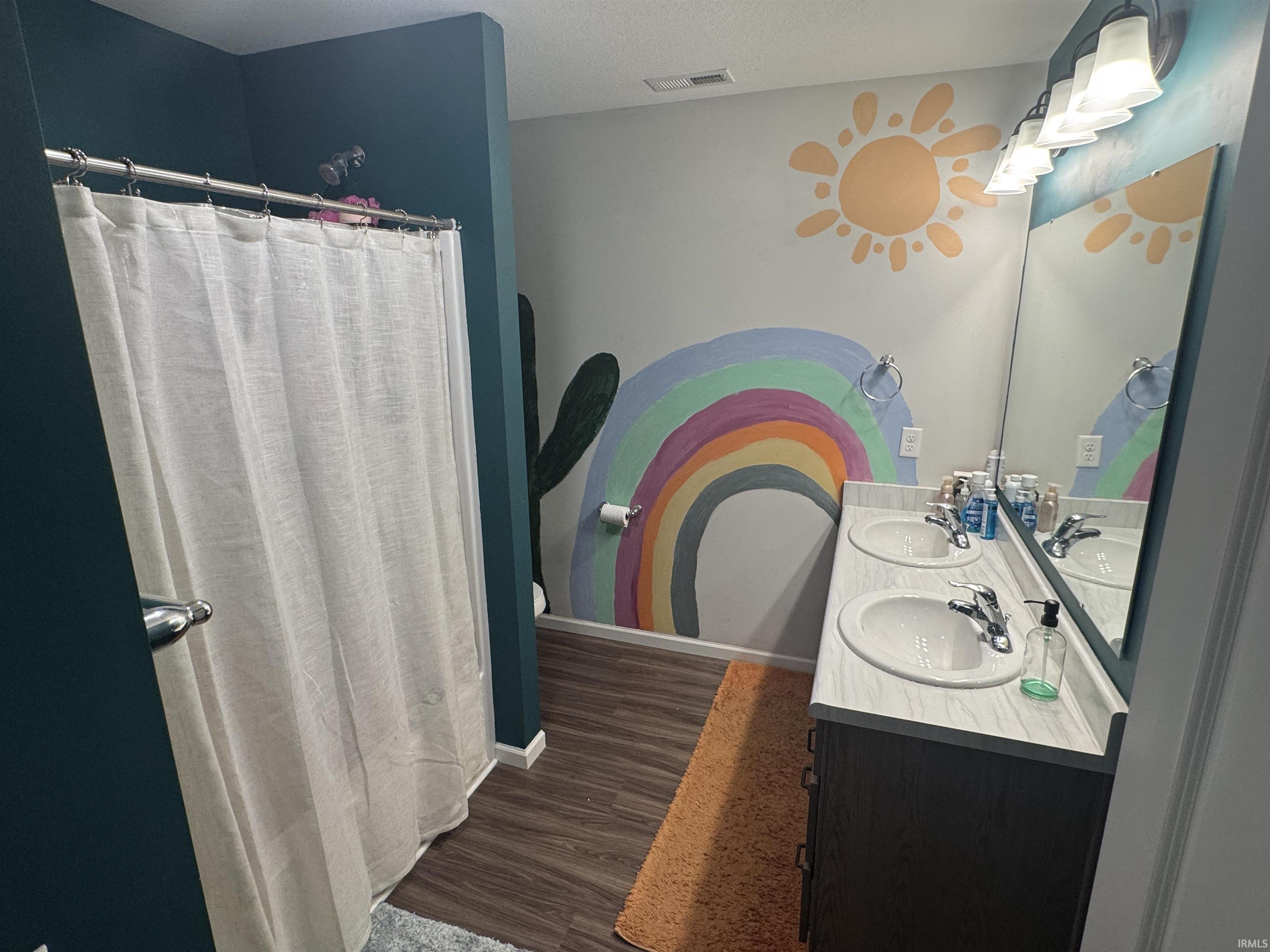 Full bath with double vanity, curtained shower, and dark wood-style flooring