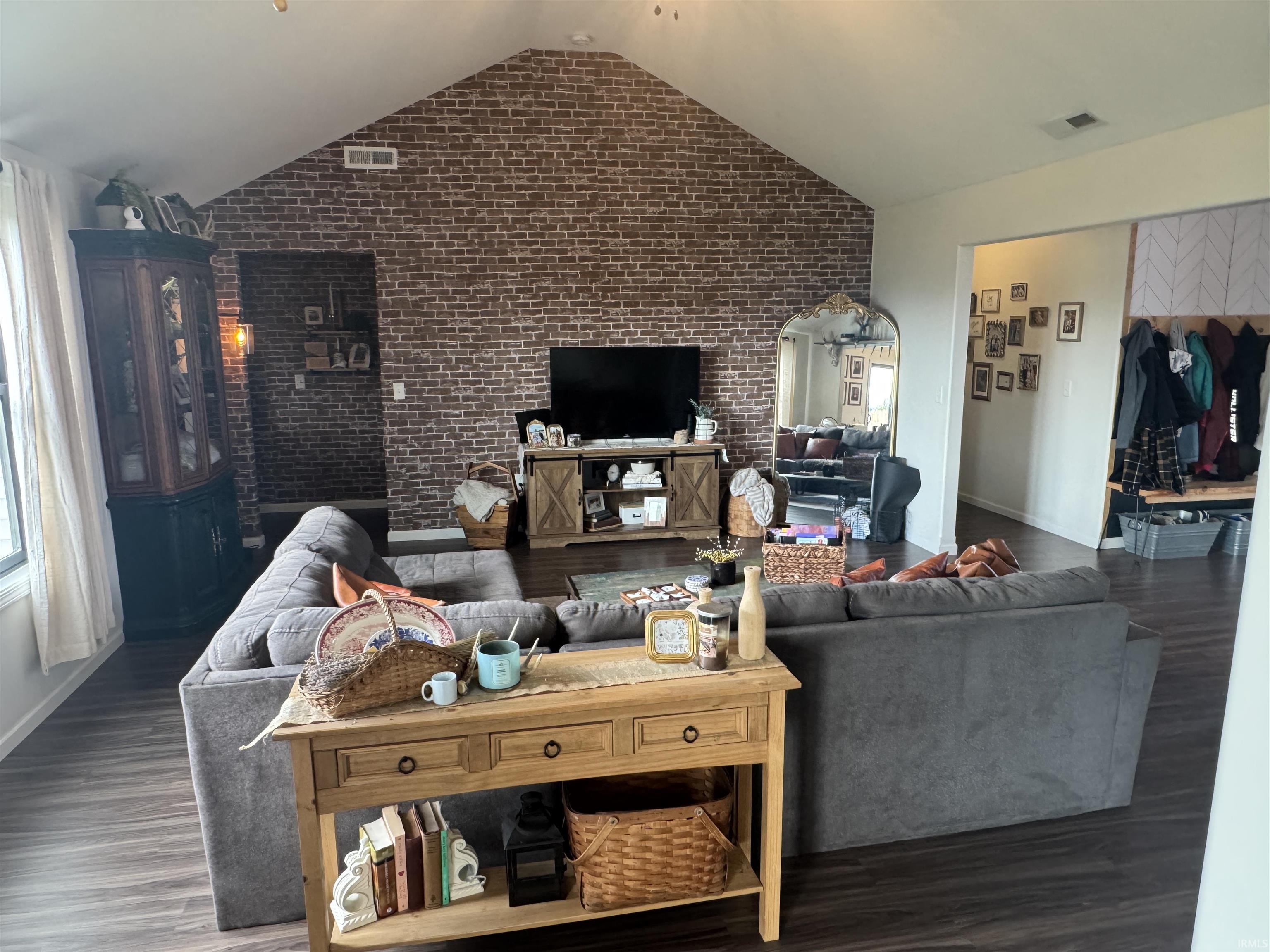 Living room featuring brick wall, wood finished floors, and a high ceiling