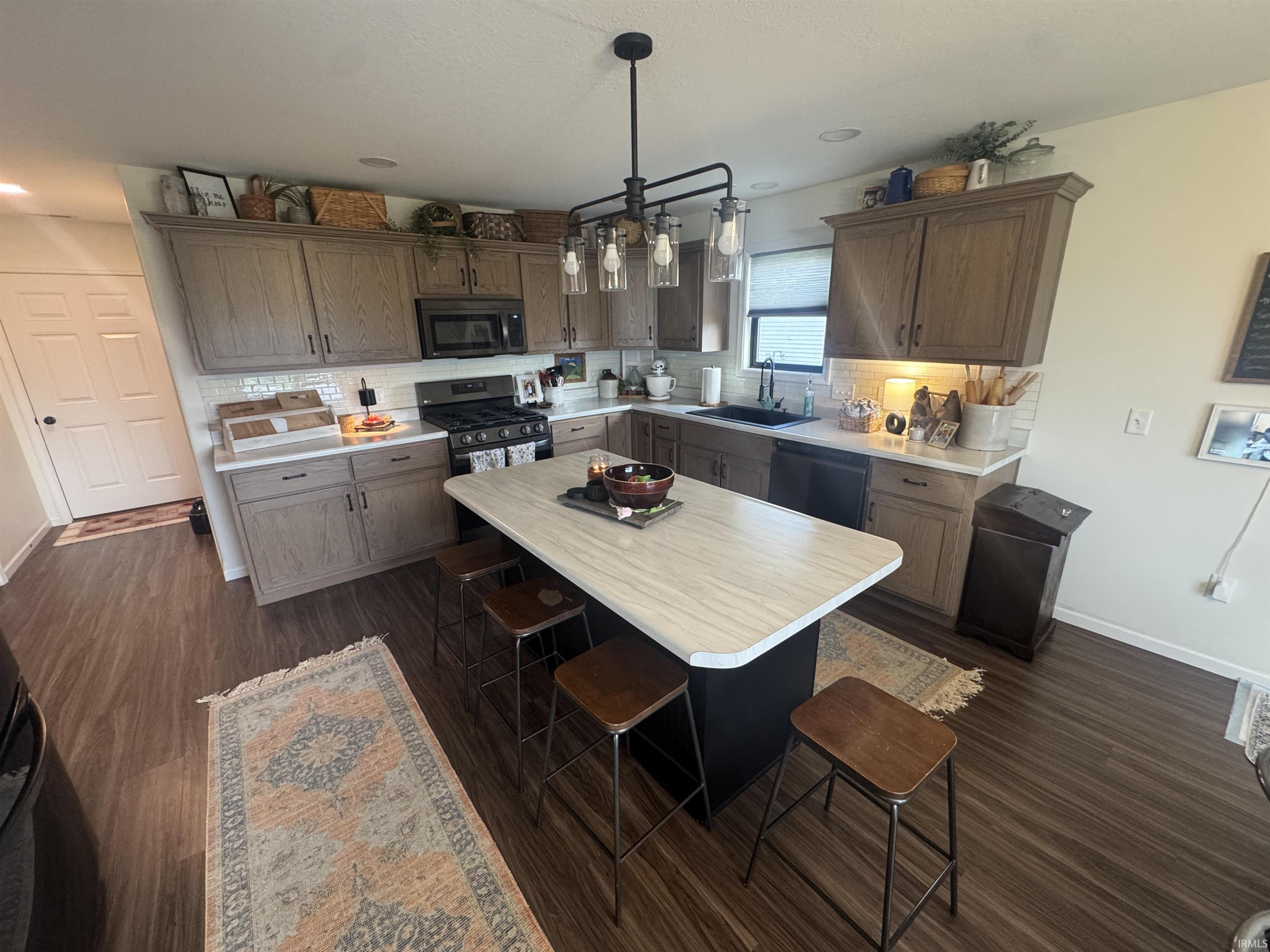 Kitchen with a breakfast bar area, light countertops, black appliances, tasteful backsplash, and dark wood-style floors