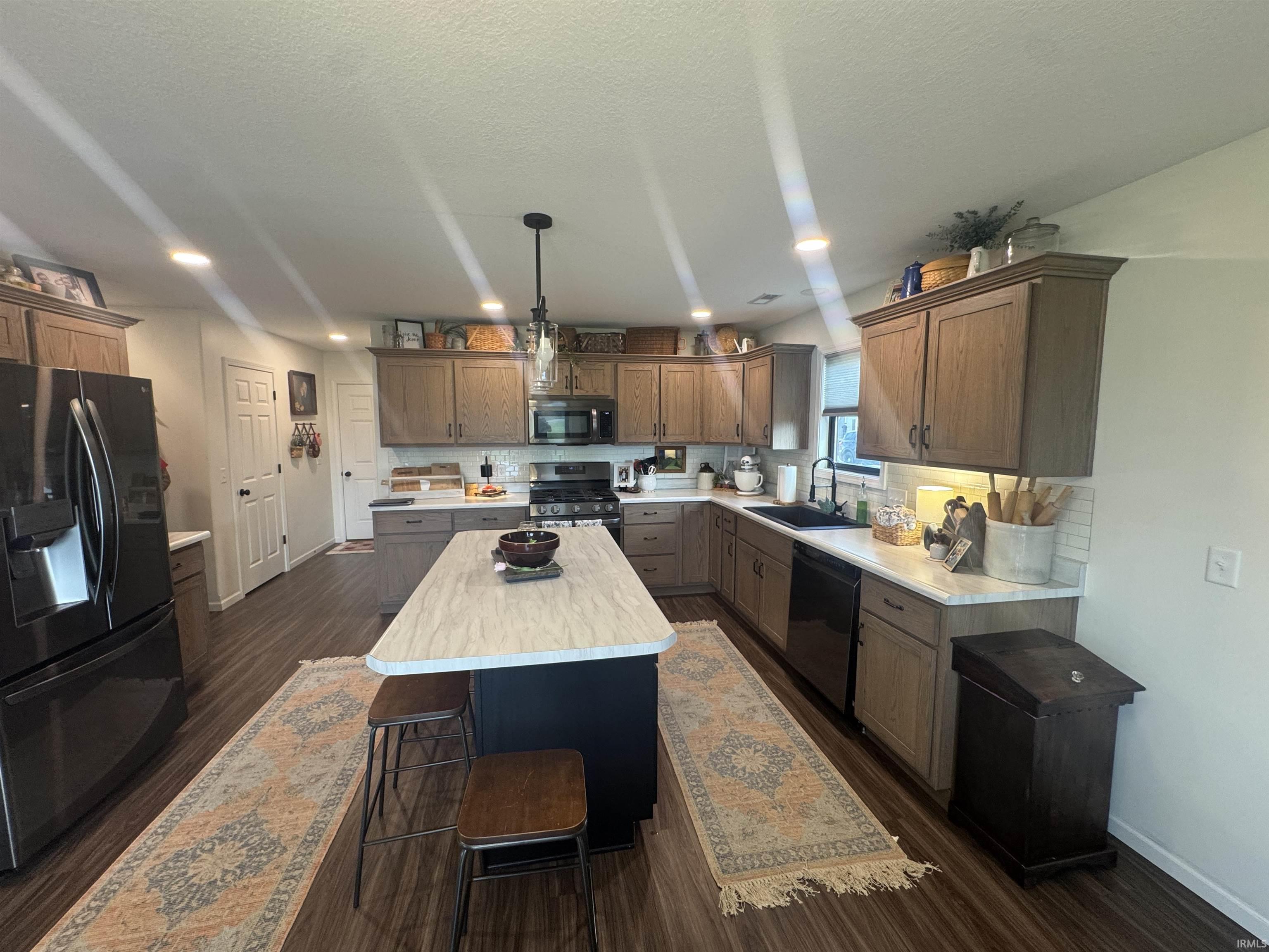 Kitchen featuring black appliances, a breakfast bar area, a kitchen island, dark wood-type flooring, and a textured ceiling