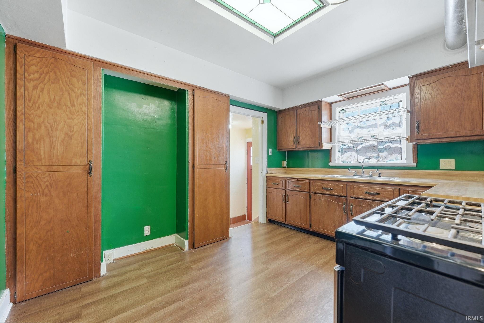 Kitchen featuring black gas range, light countertops, wood finish cabinets, light wood-type flooring, and a skylight