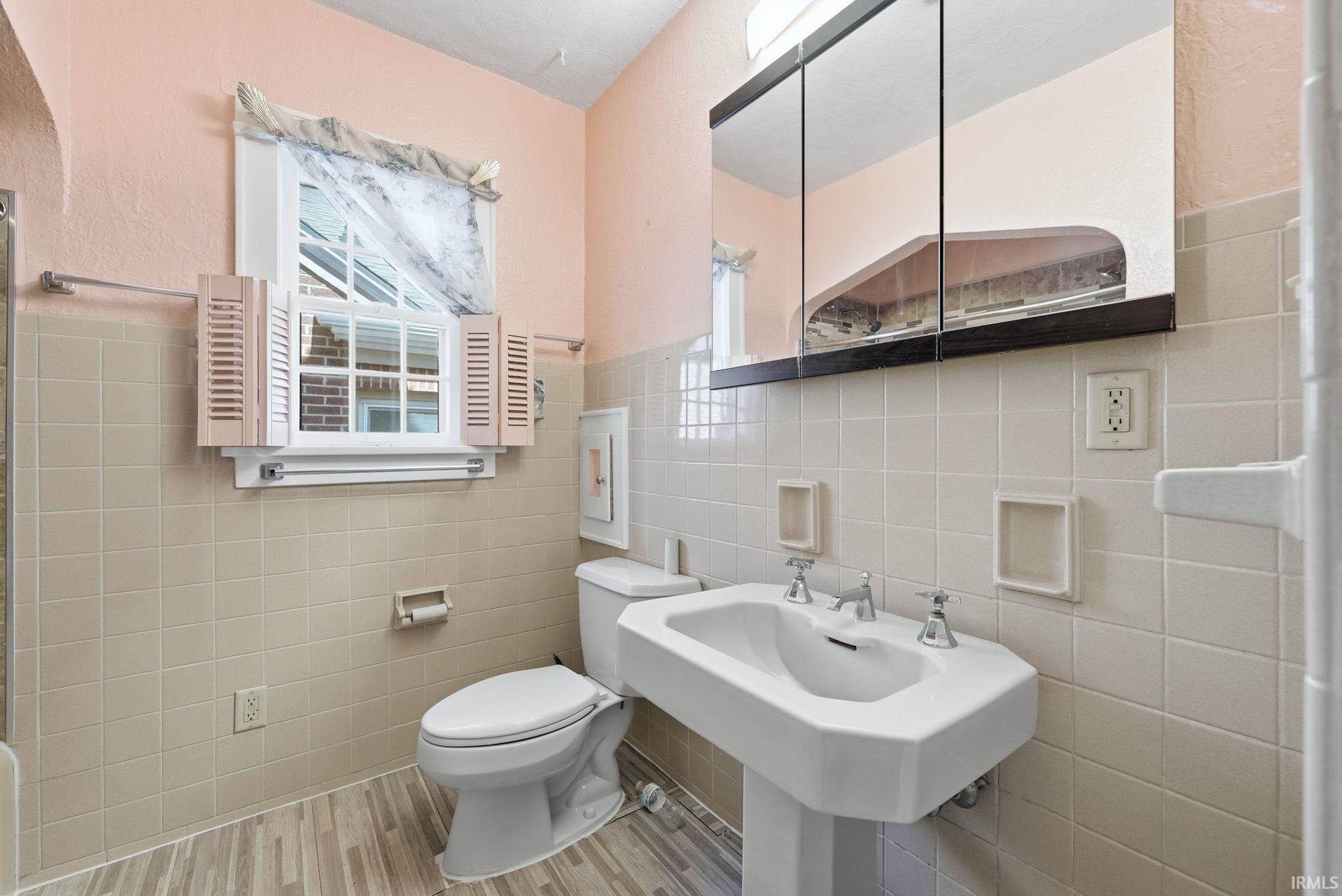 Full bathroom with tile walls, wainscoting, a textured wall, and light wood finished floors