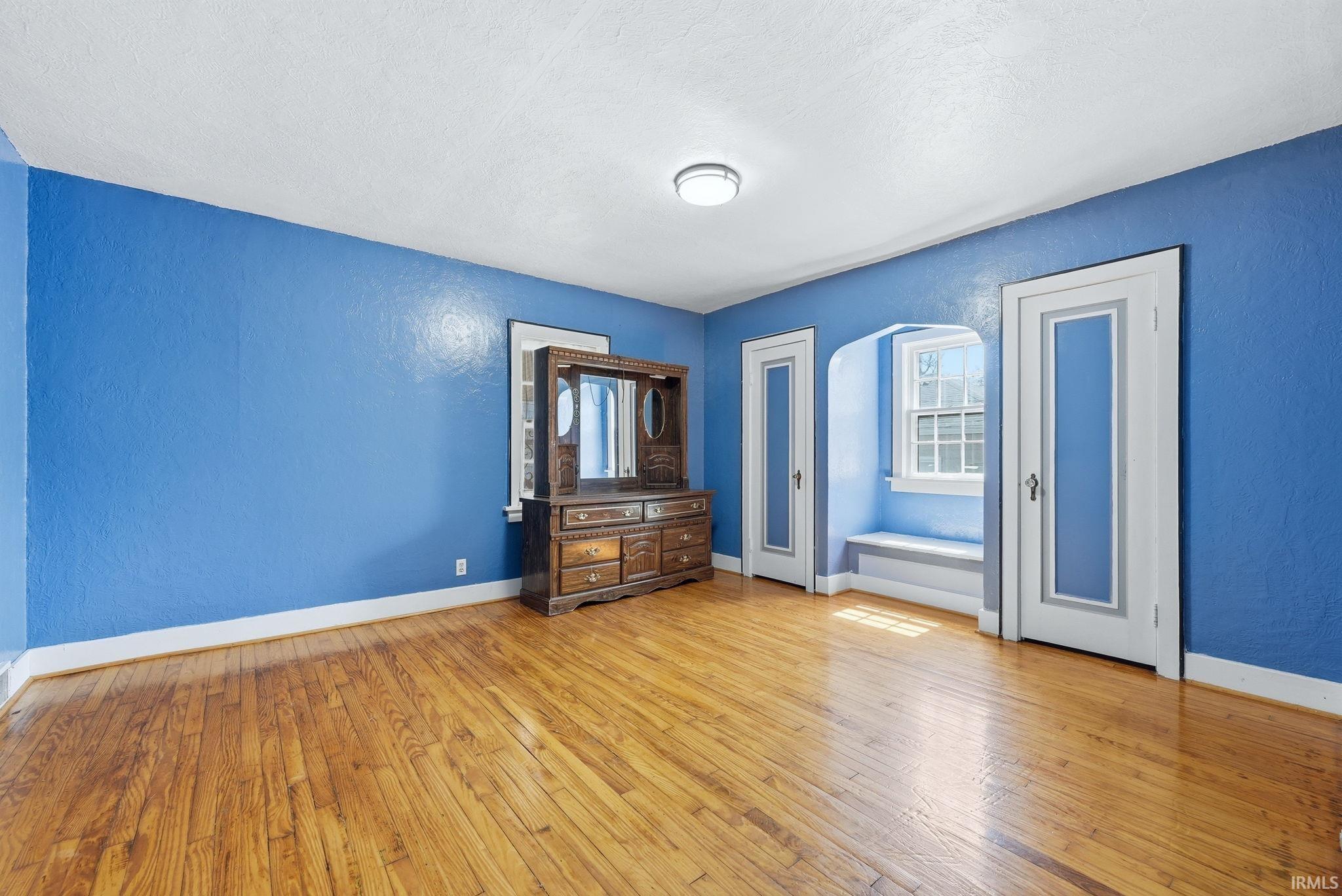 Unfurnished bedroom featuring a textured wall, light wood-style flooring, arched walkways, multiple closets, and a textured ceiling