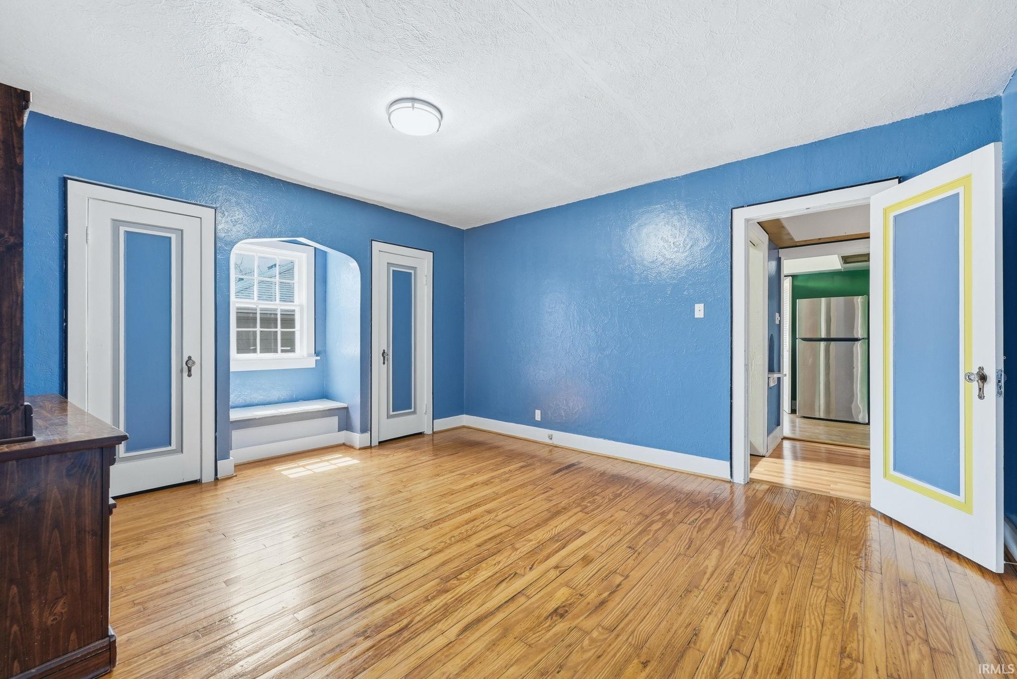 Unfurnished living room with light wood-style flooring, arched walkways, a textured ceiling, and a textured wall