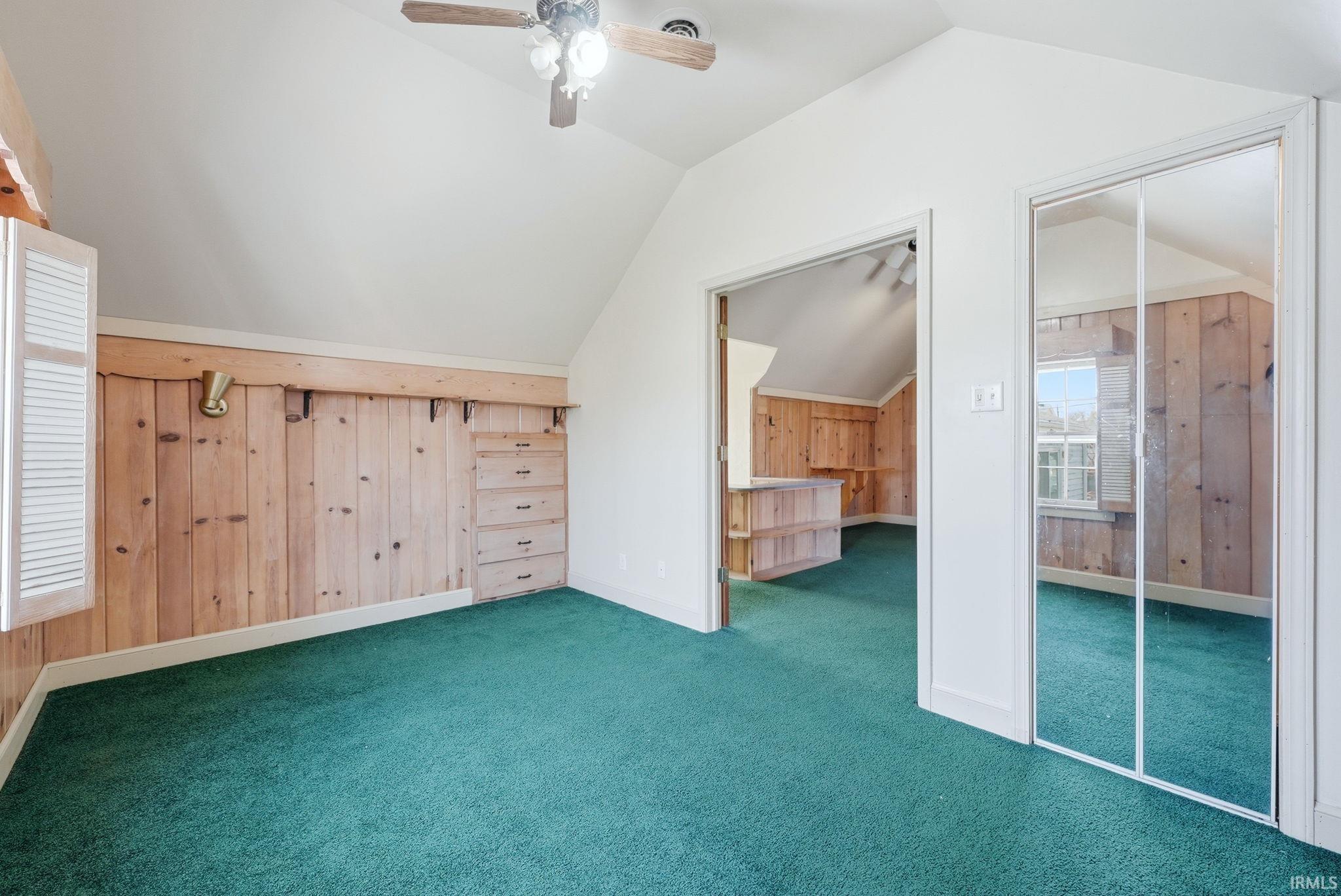 Bonus room with wooden walls, lofted ceiling, ceiling fan, and carpet floors
