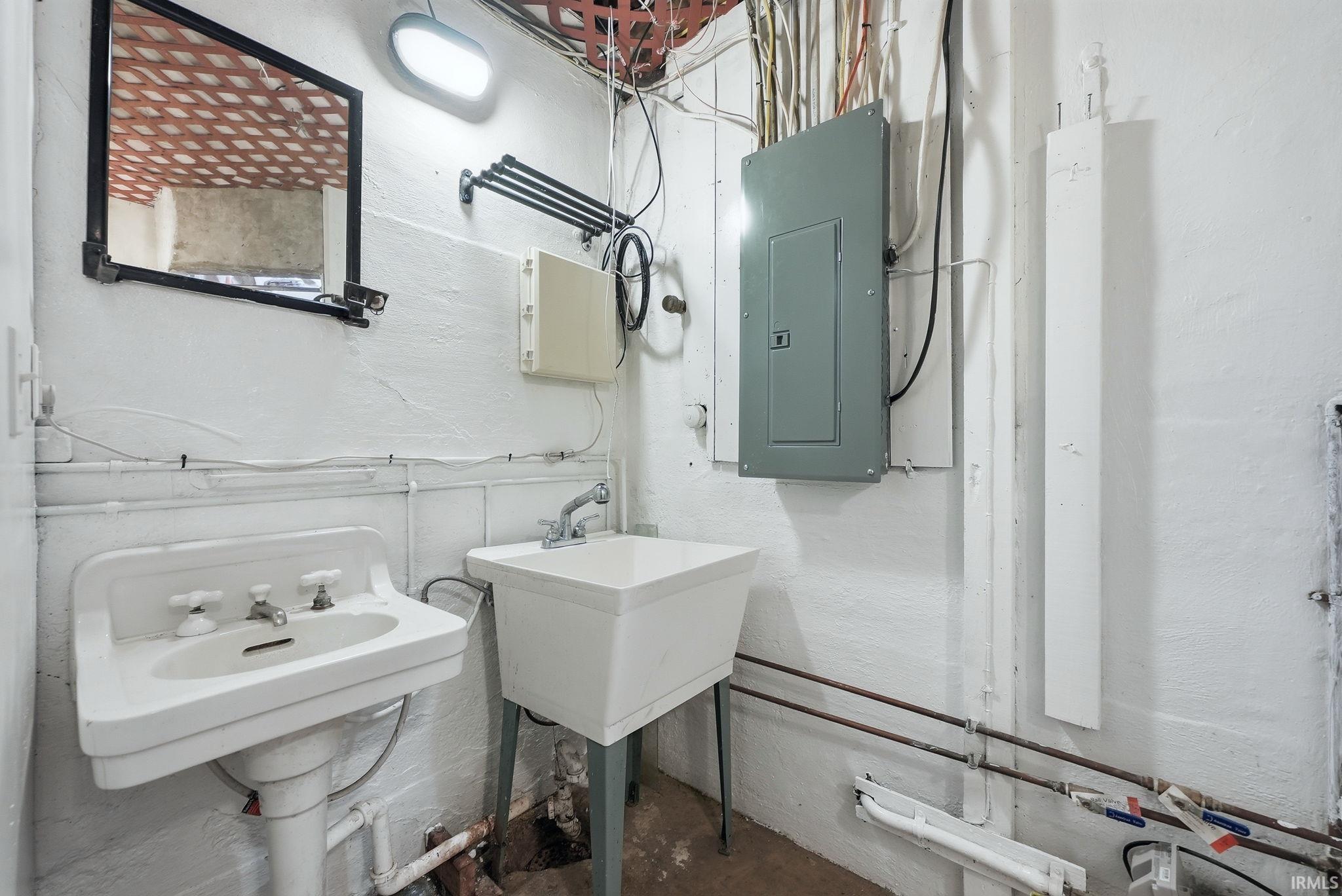 Bathroom with electric panel, unfinished concrete floors, and two sinks