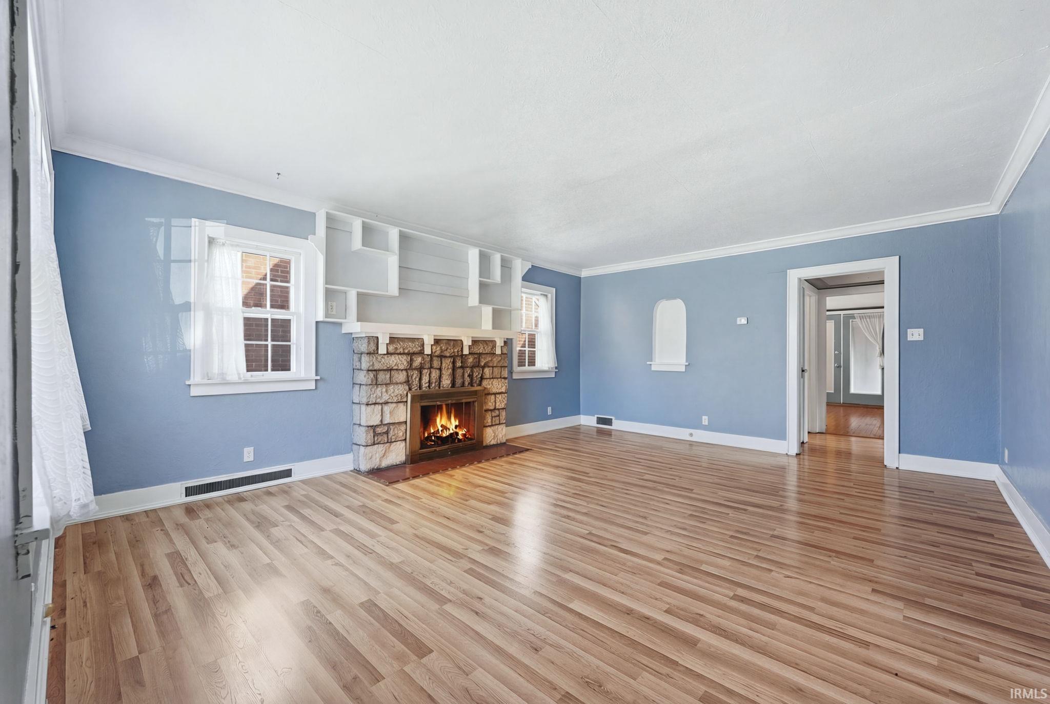 Unfurnished living room with crown molding, light wood-style floors, and a fireplace