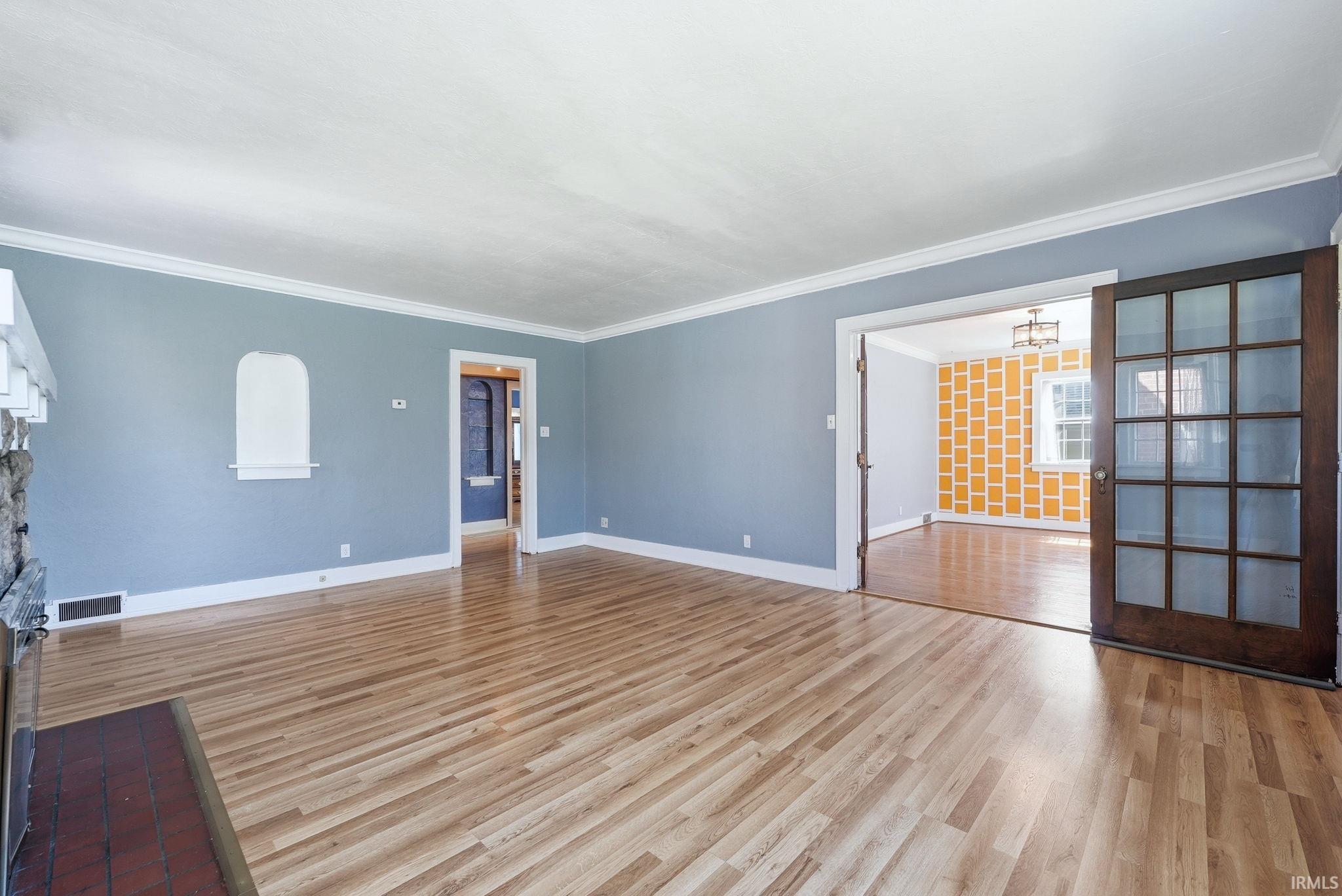 Unfurnished living room featuring light wood finished floors, ornamental molding, and hanging lights