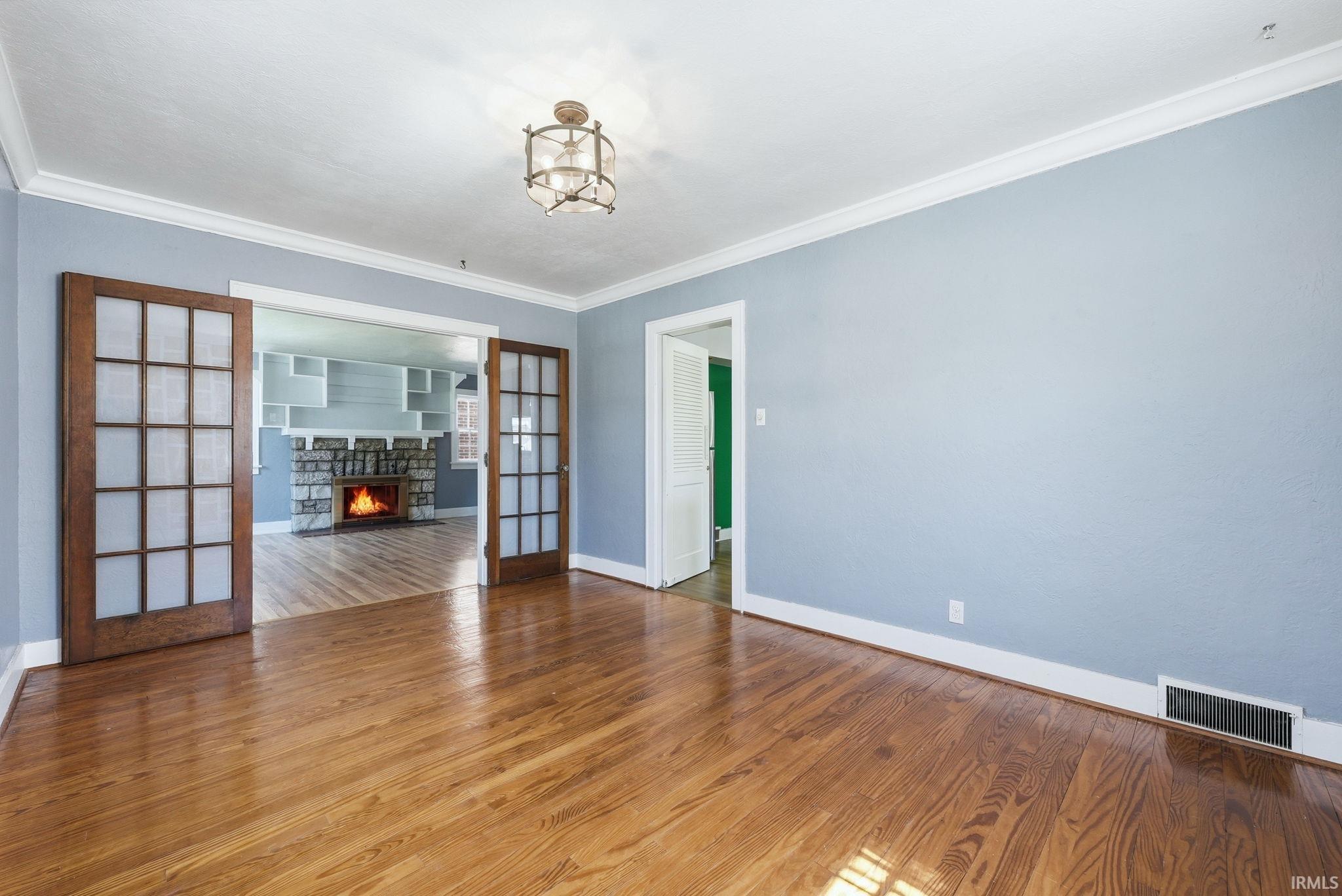 Unfurnished room featuring a fireplace, hardwood / wood-style flooring, crown molding, and french doors
