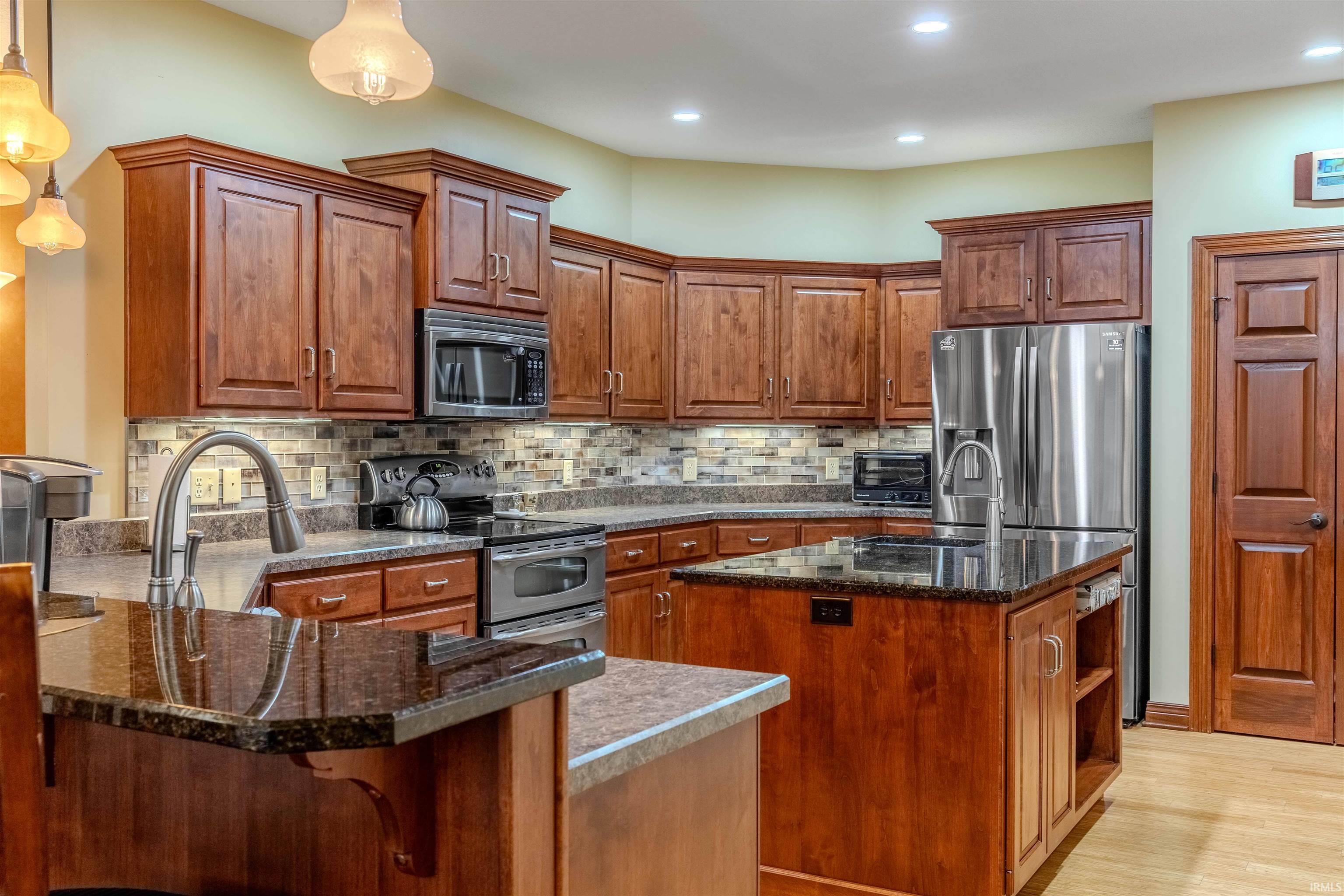 Custom Kitchen featuring stainless steel appliances, dark granite counters, a peninsula w/island, Grabill hand crafted cabinets, and custom backsplash