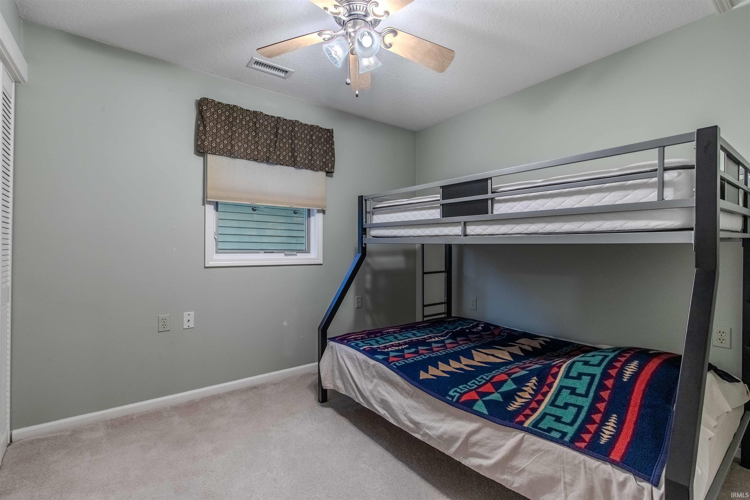 Bedroom with light carpet, ceiling fan, and a textured ceiling. This BR has the crawl space access to sump pump, etc in closet.