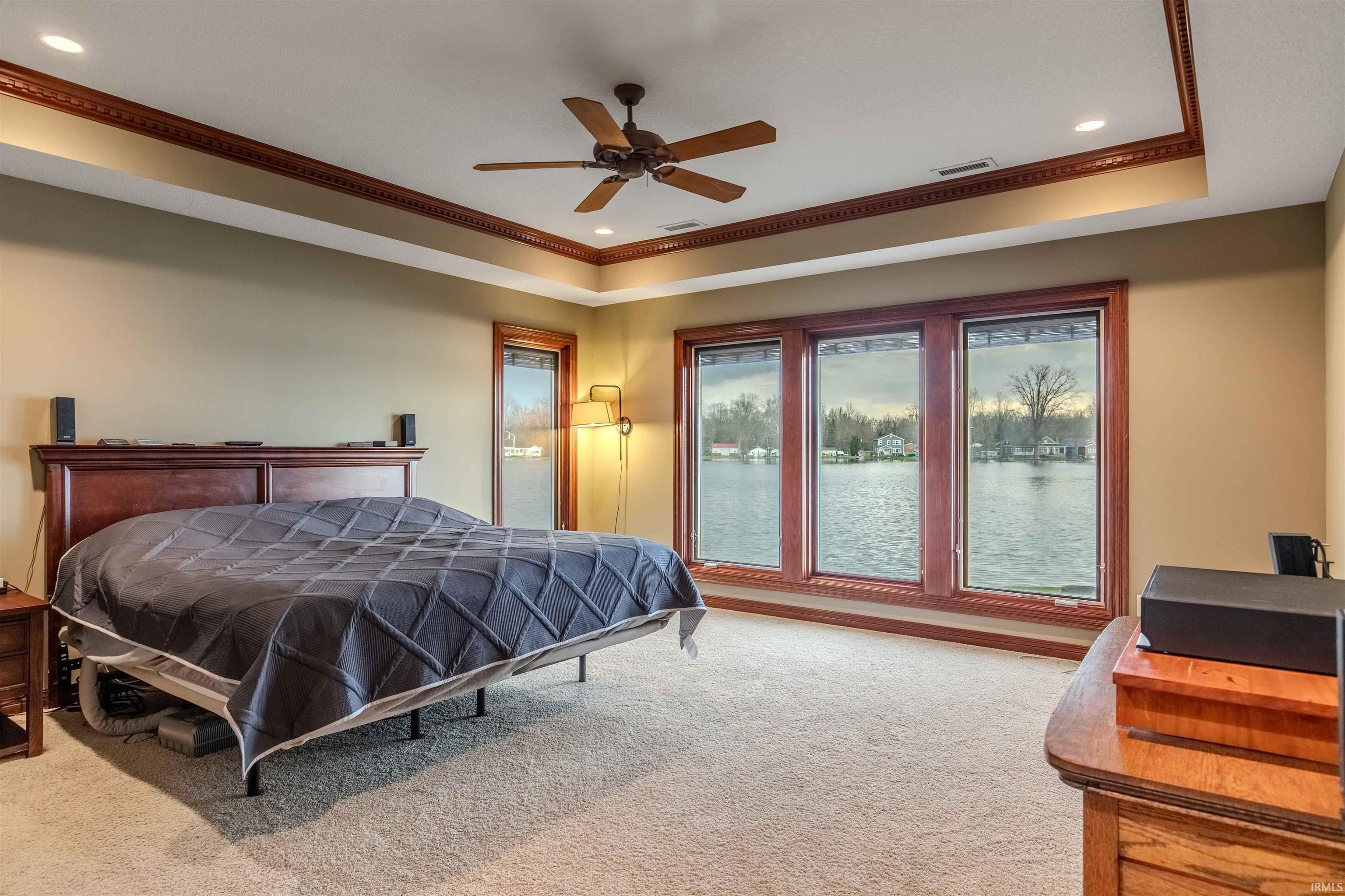 Featuring a tray ceiling, ornamental custom moldings, recessed lighting, and a stunning view of the lake to wake up to.