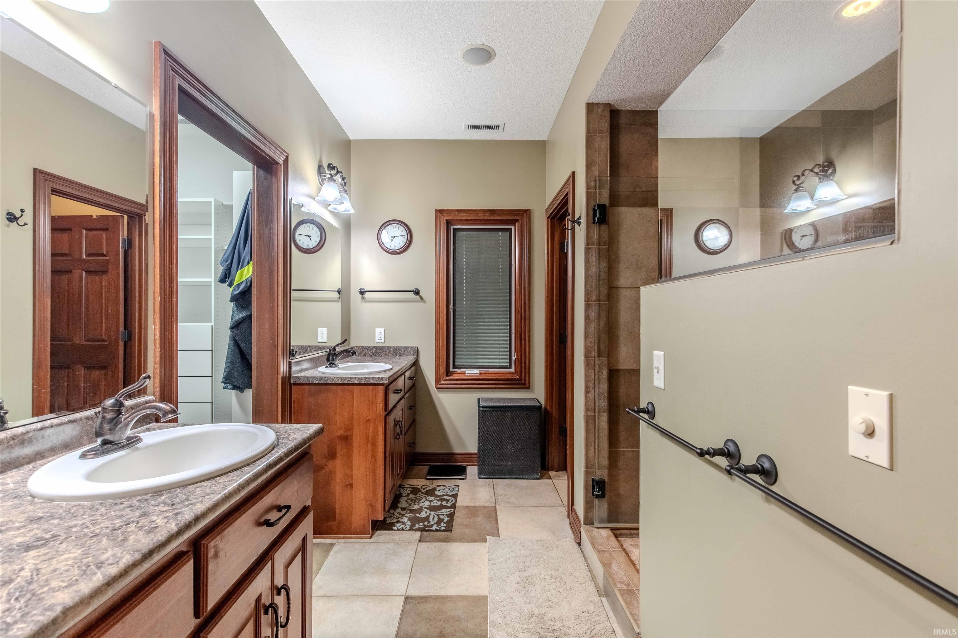 Custom design bath with heated tile floors, tiled shower, two vanities, and Travertine style tile patterned flooring.