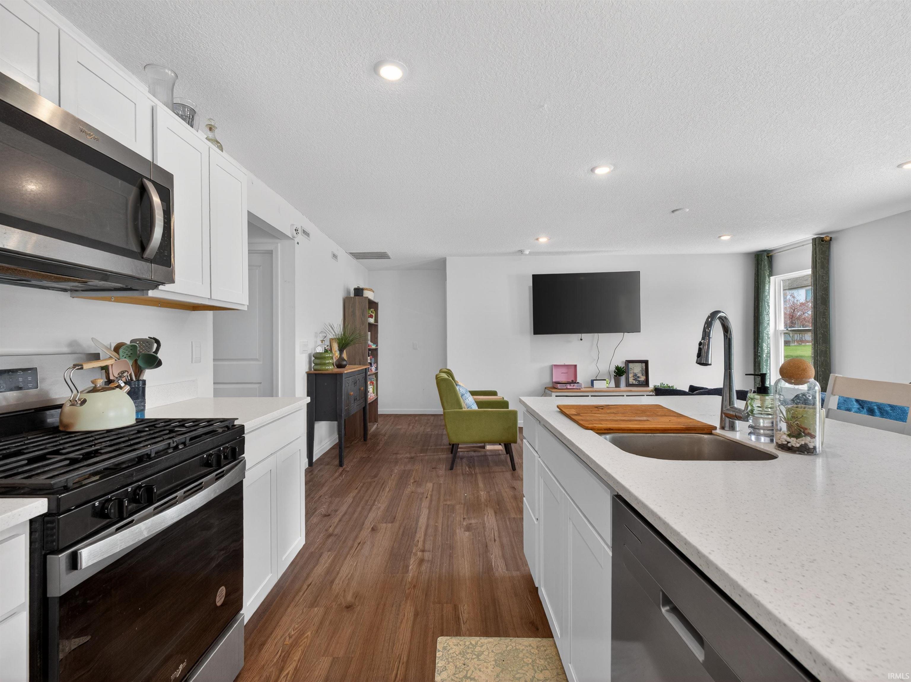 Kitchen featuring stainless steel appliances, white cabinets, light stone counters, dark wood-style flooring, and recessed lighting