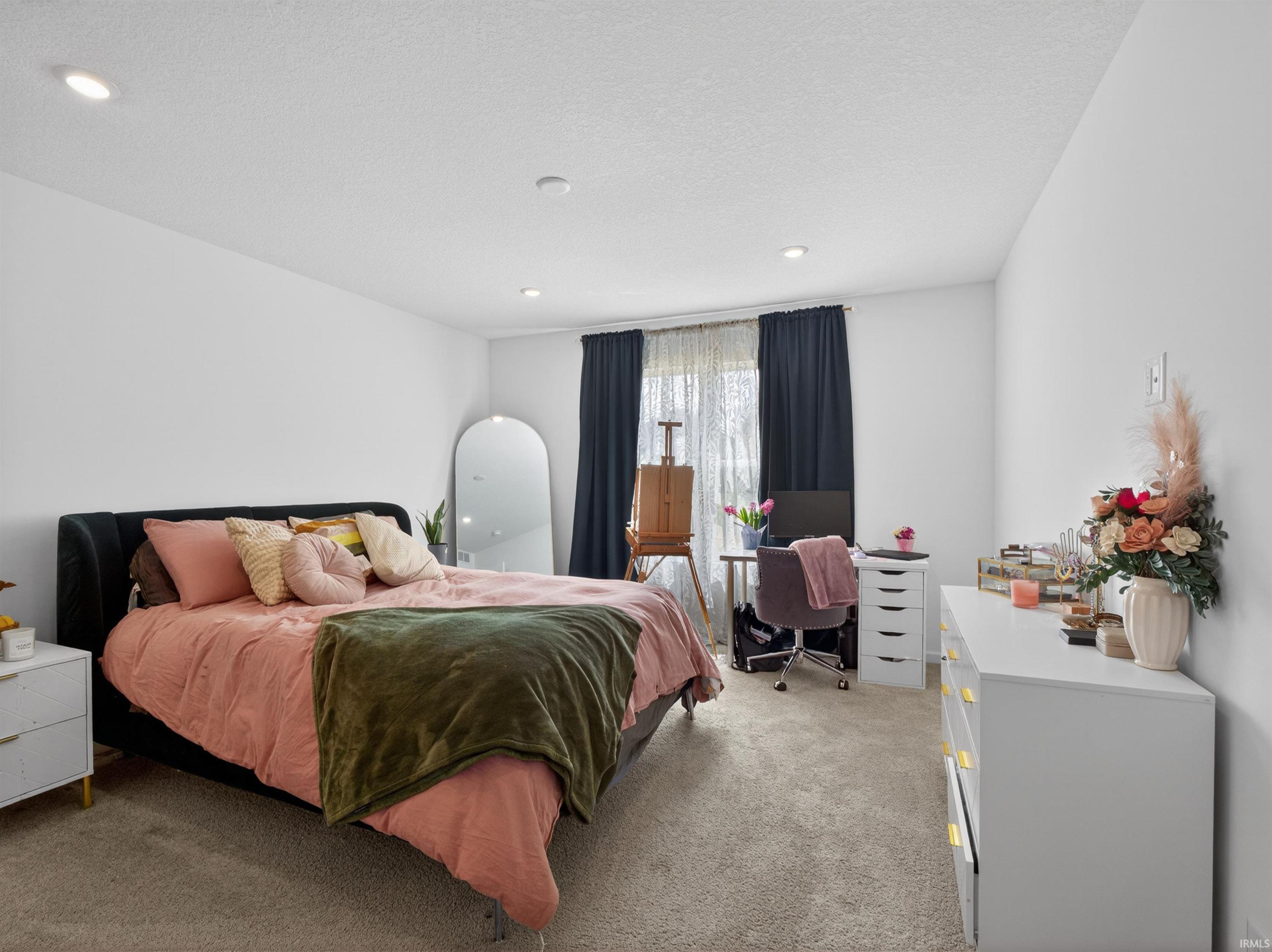Bedroom with light colored carpet, a textured ceiling, and a desk