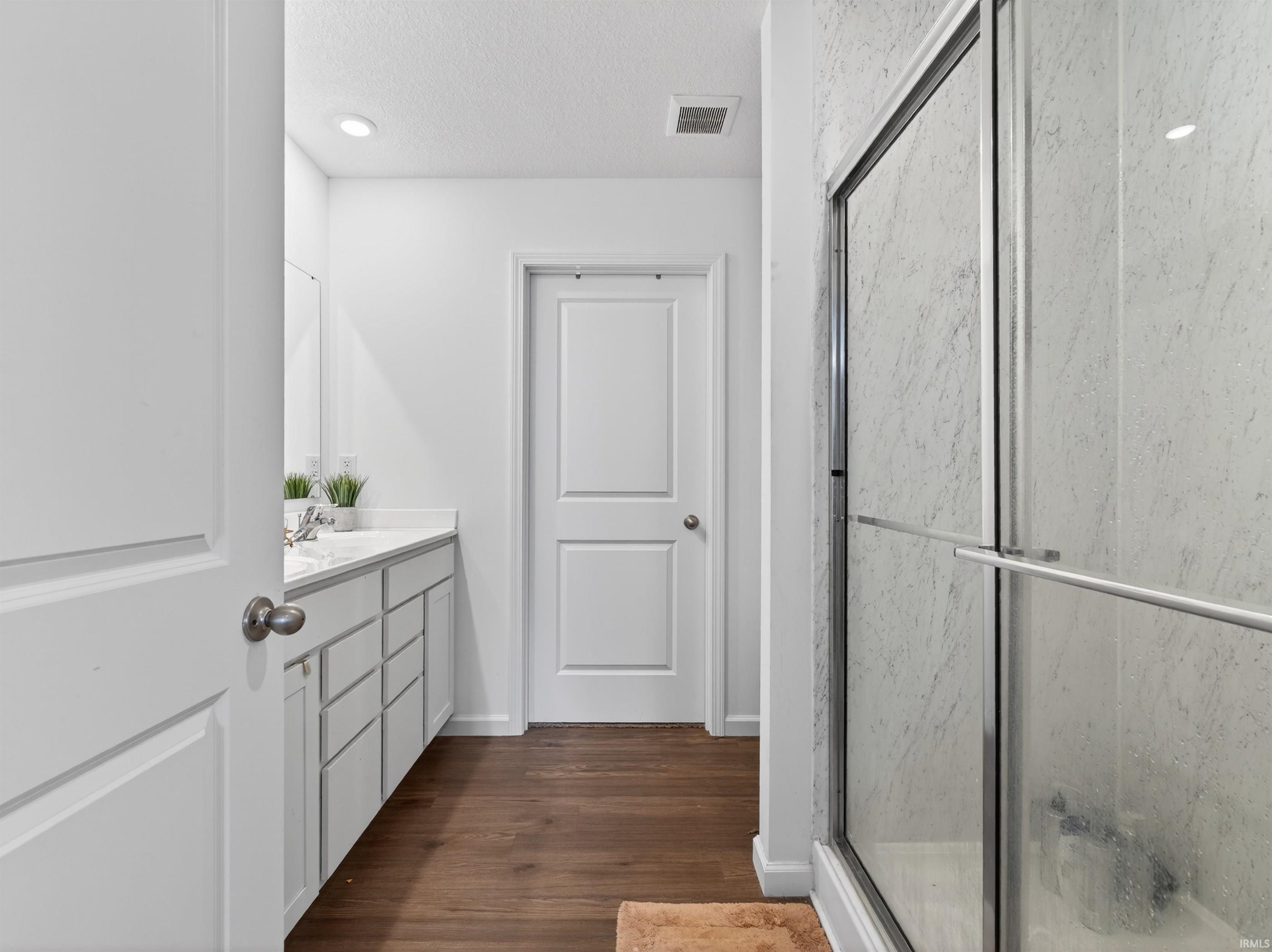 Bathroom featuring a textured ceiling, vanity, a shower with shower door, and dark wood finished floors