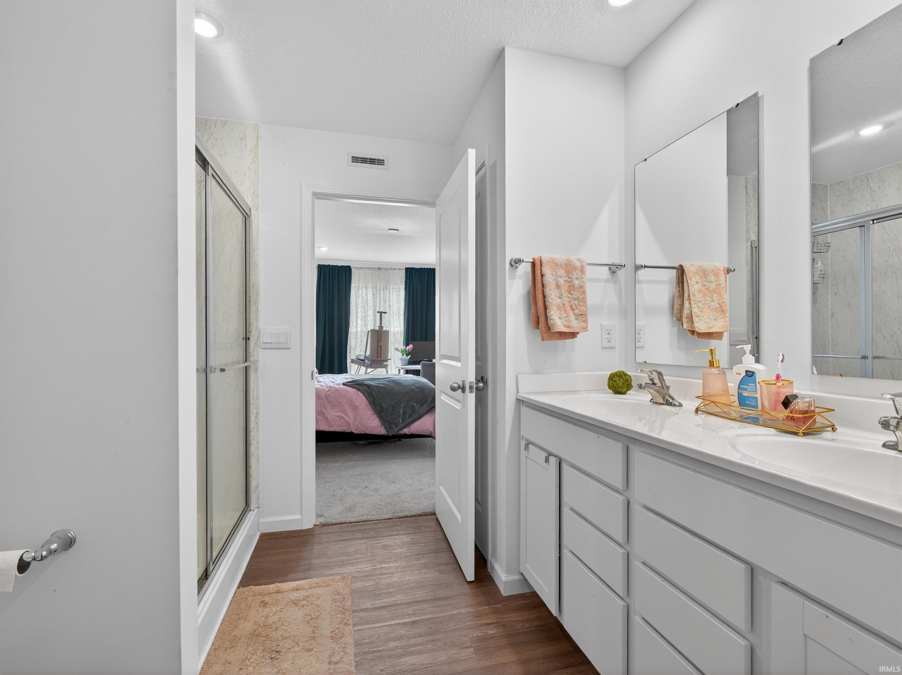 Full bathroom with double vanity, a shower stall, connected bathroom, and dark wood-style floors