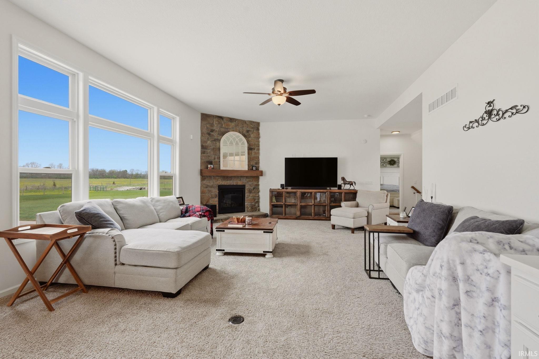 Living room featuring light colored carpet, ceiling fan, and a stone fireplace