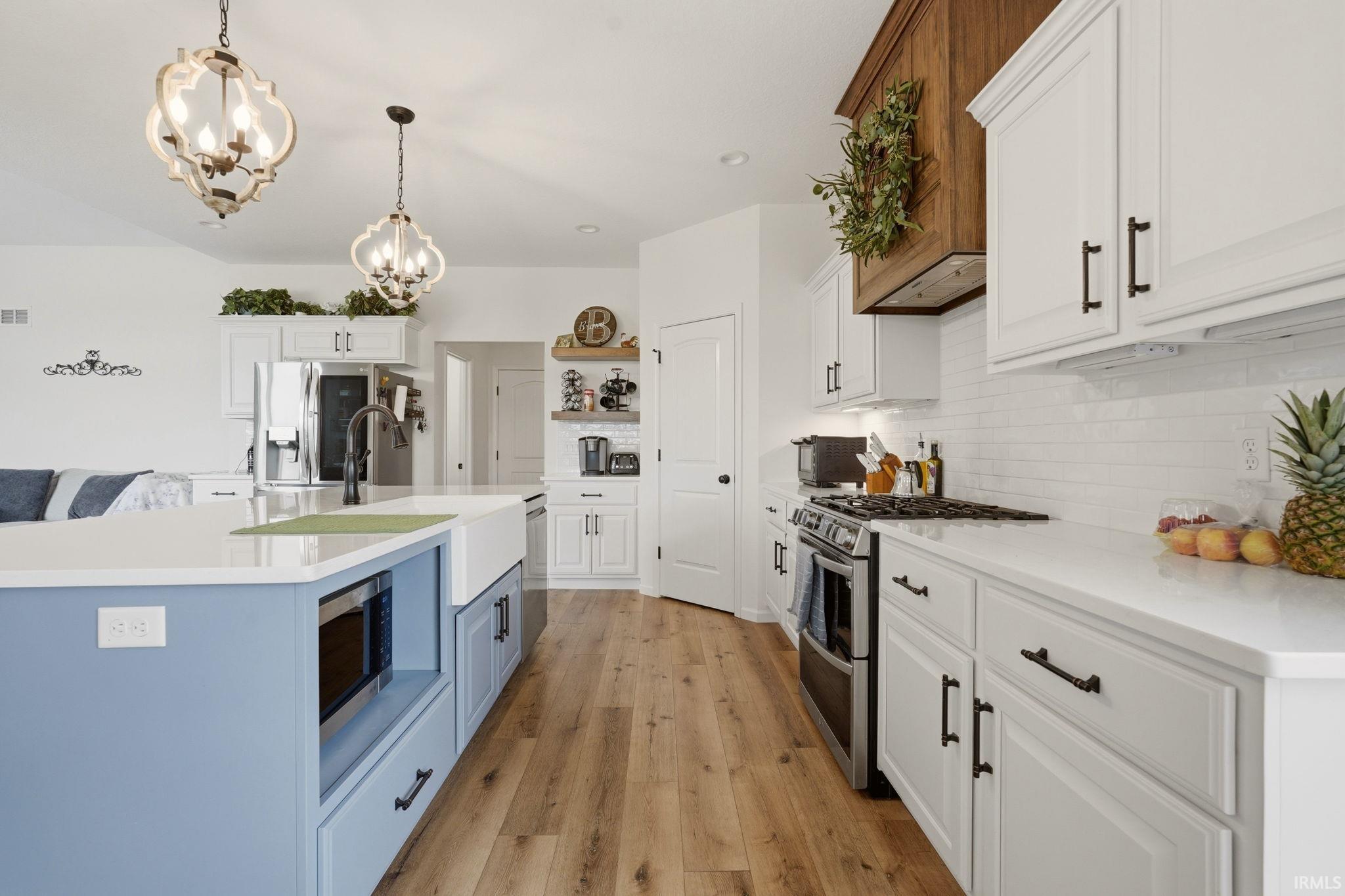 Dual tone kitchen with dual tone cabinets, stainless steel appliances, hanging lights, light wood finished floors, and open shelves