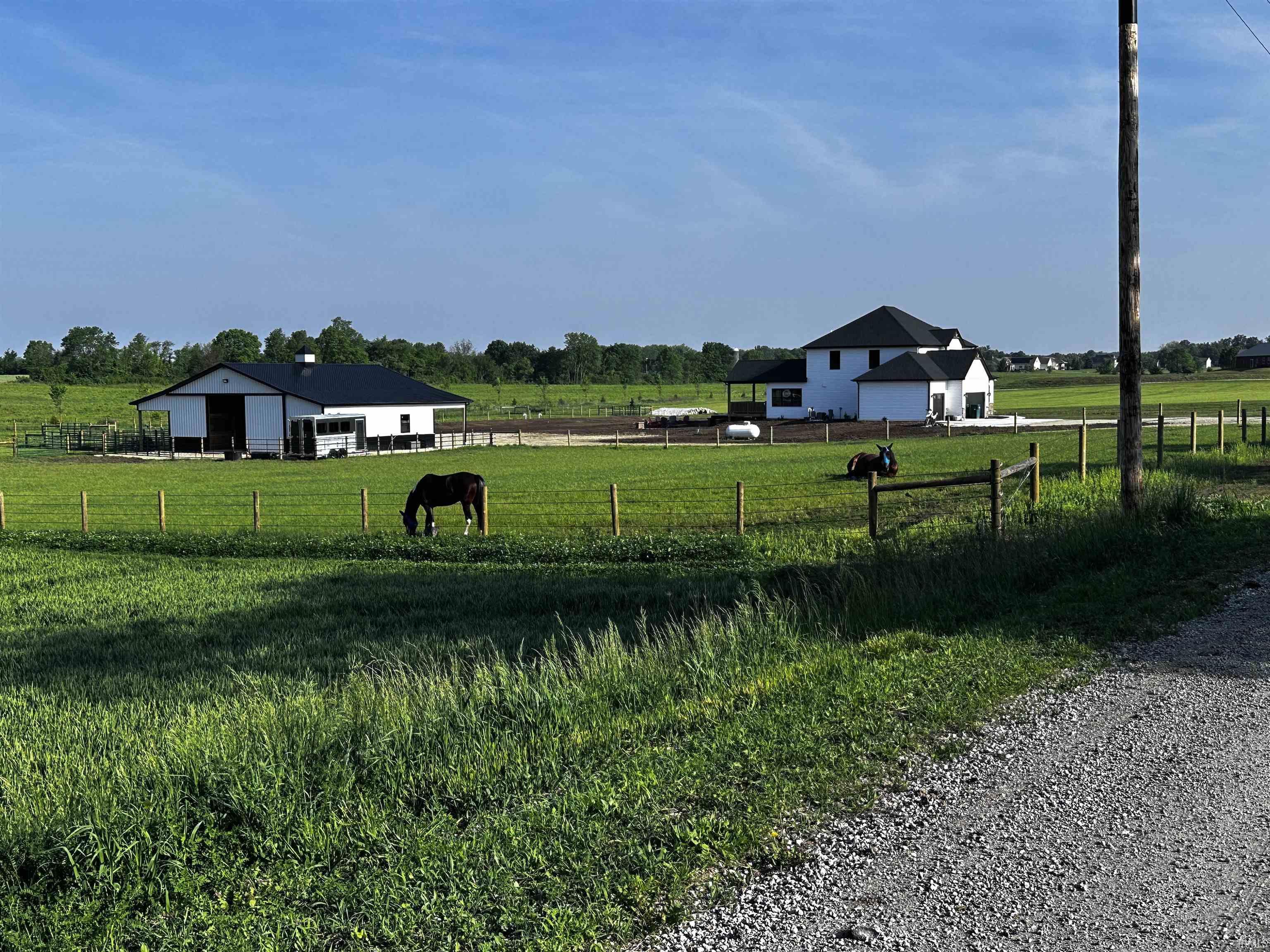 Expansive fenced acreage featuring a white residence with dark roofing, a white barn with dark roofing, and a gravel road frontage