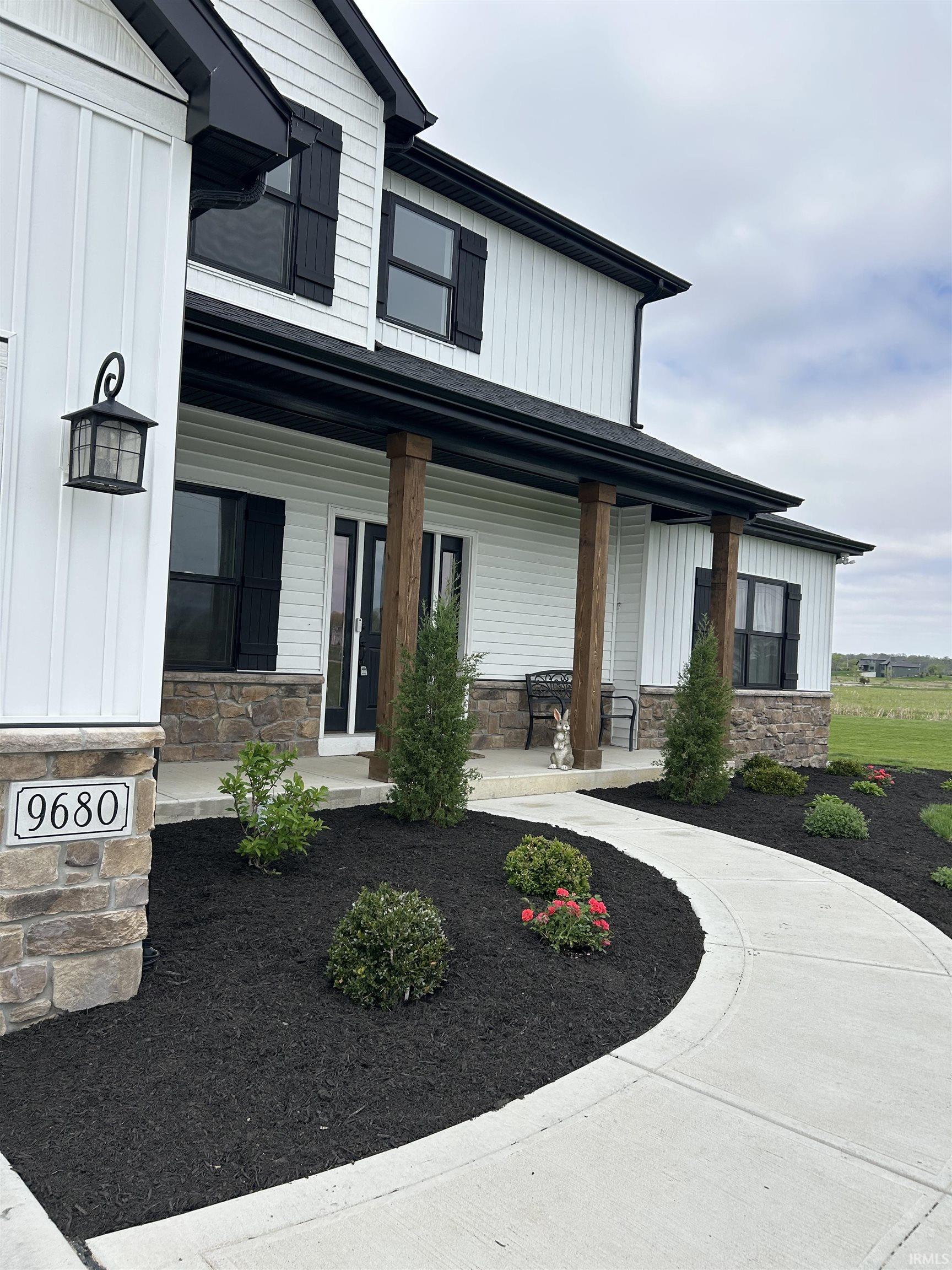 Two-story residence featuring white board and batten siding, black window shutters, and a stone facade foundation