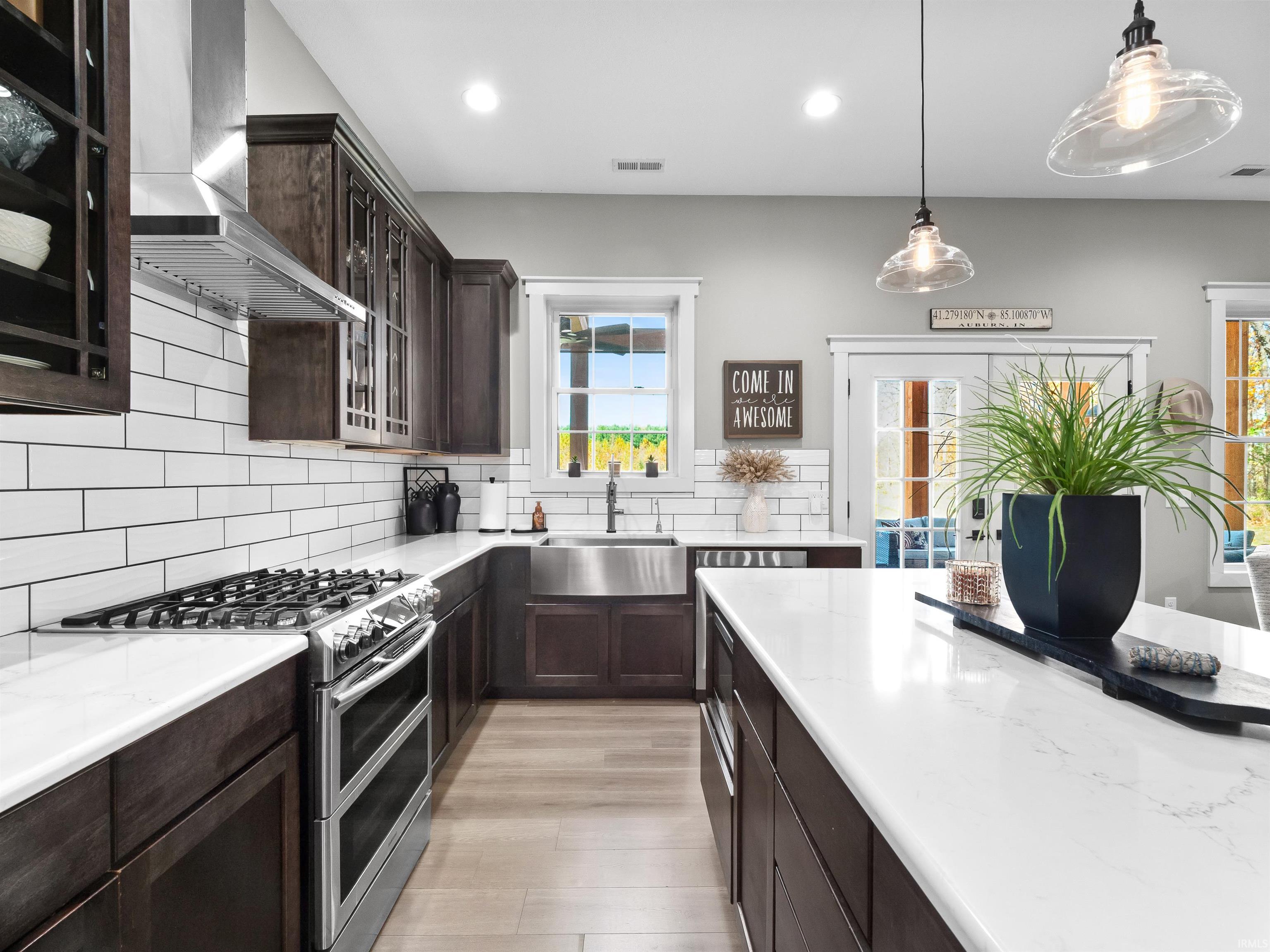 Kitchen with dark wood finish cabinetry, glass insert cabinets, double oven range, and backsplash