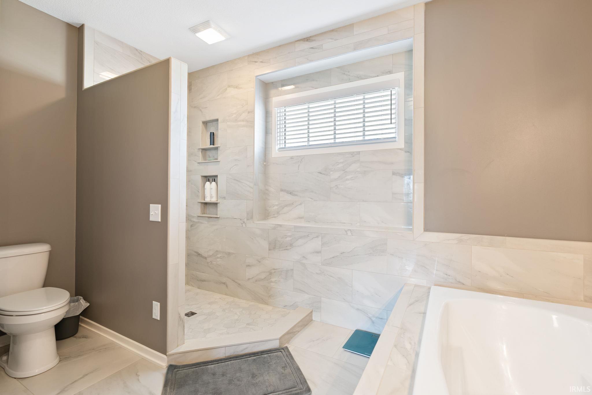 Bathroom with marble look tiles, a marble finish shower, and a garden tub