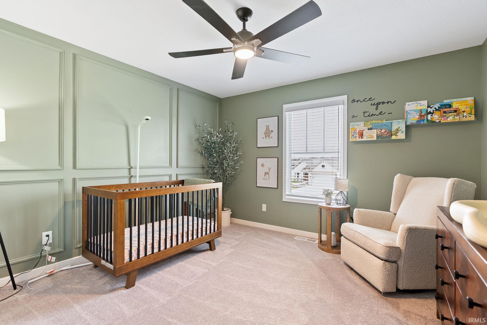Bedroom with a decorative wall, a crib, light carpet, and ceiling fan